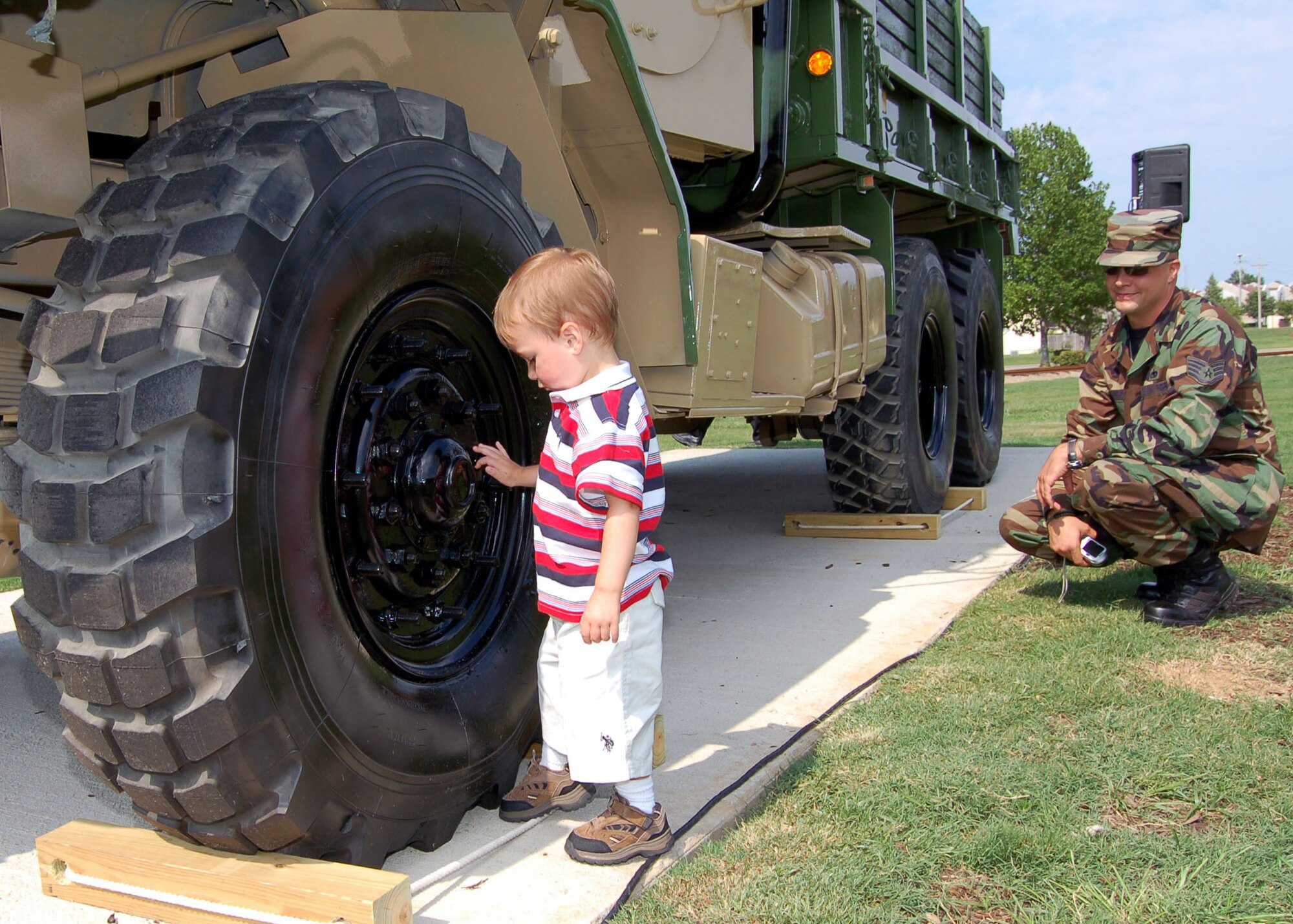 Staff Sgt. Brian Hanson, 1st Special Operations Logistics Readiness Squadron, watches his 2-year-old son, Christopher, check out the tire of a convoy gun truck shortly before it was dedicated as a static display at the Maxwell Air Force Base's Gunter Annex, Ala. (USAF Photo by Master Sgt. Lee Roberts)