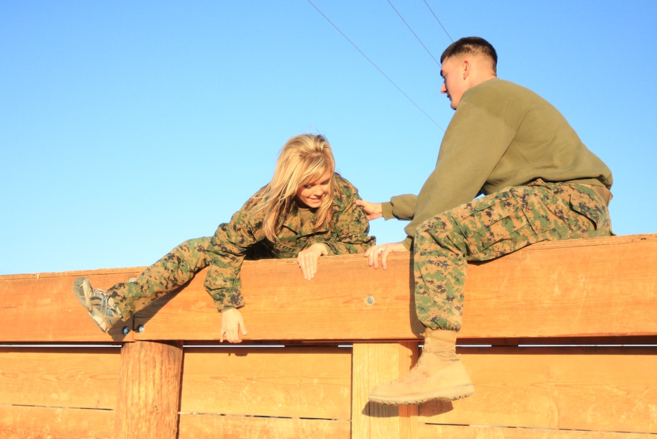 Jennifer Pelletier, who participated in 2nd Battalion, 7th Marine Regiment’s Jane Wayne Day, climbs over the obstacle course wall with a little help Nov. 19.