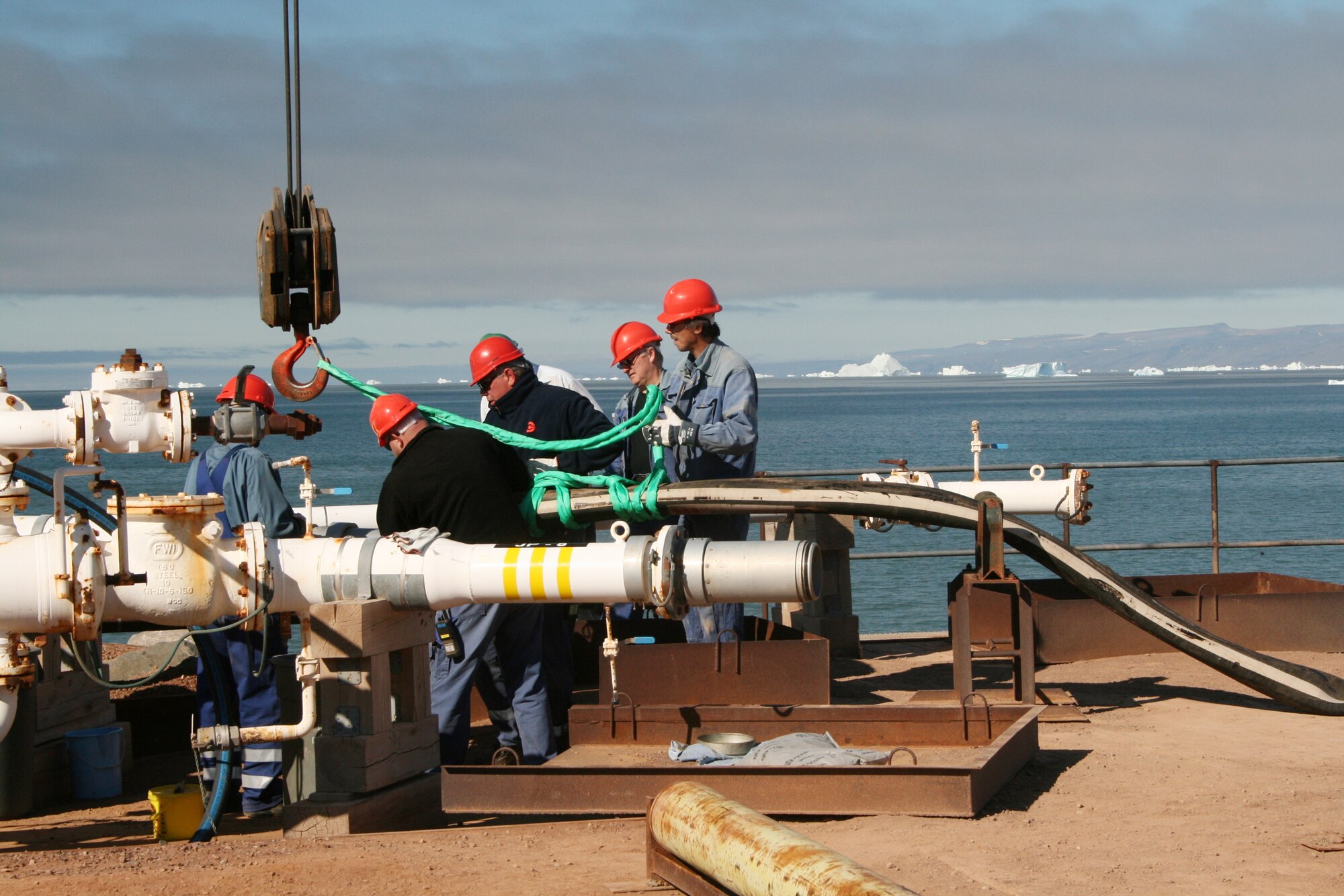 Icebergs are visible in the distance as workers connect fuel supply lines on the pier from the Motor Vessel Marvea. The crew offloaded 8.8 million gallons of JP-8 diesel fuel and 80,000 gallons of unleaded fuel from the Marvea. Thule Air Base is reliant on the resupply ship’s cargo to survive the months-long winters in Greenland. (U.S. Air Force photo)