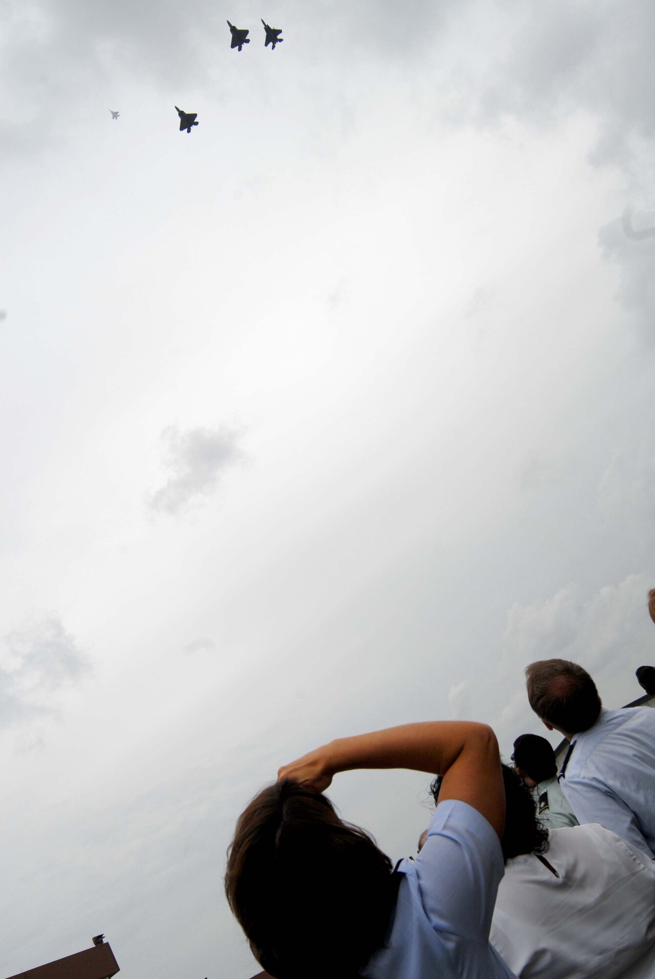 Onlookers gaze skyward as the F-22 Raptors and F-15 Eagles from the  325th Fighter Wing fly a "Missing Man" formation over the ribbon cutting ceremony for "America's AOC".