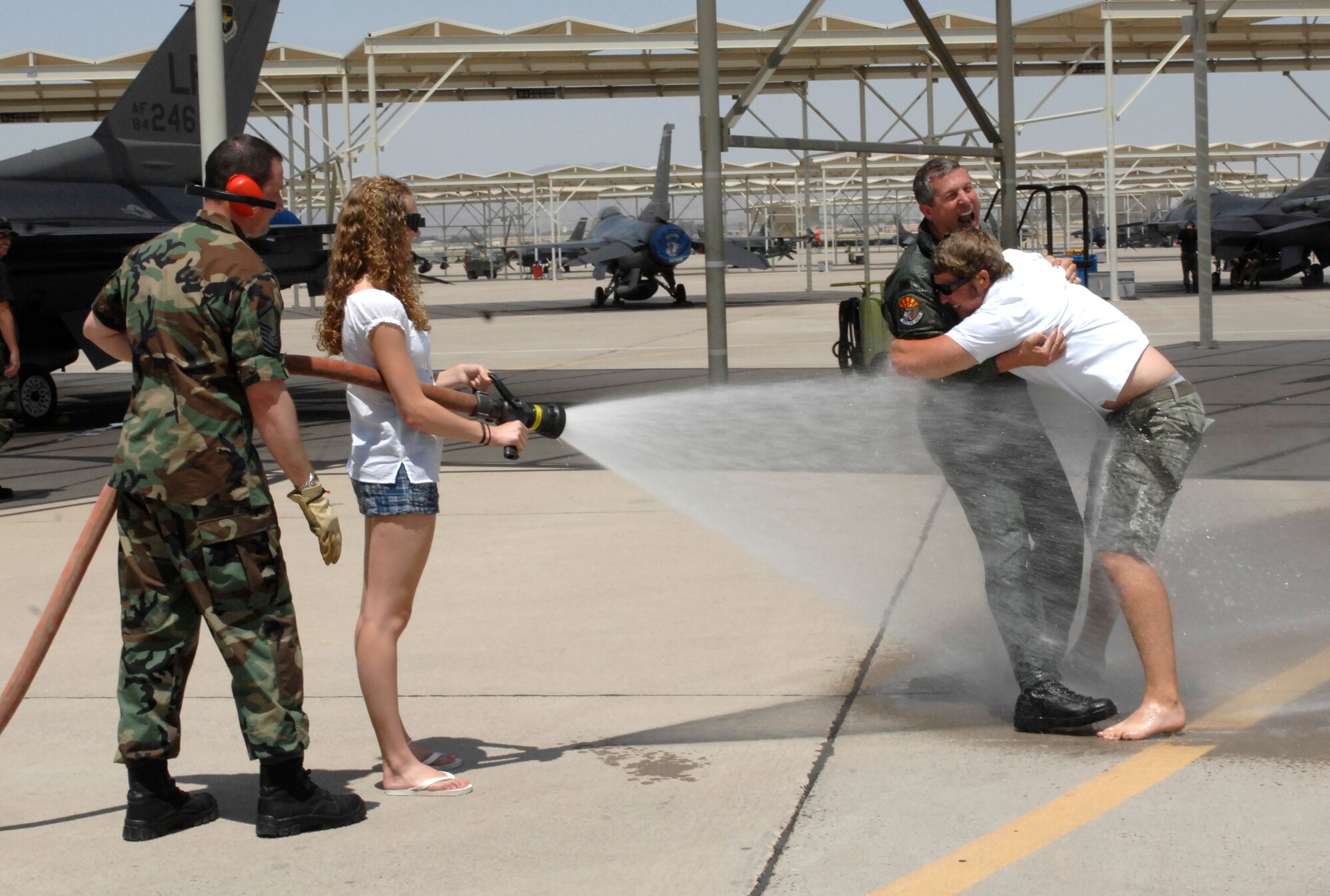 Master Sgt. Keith Berthiaume, 56th Civil Engineer Squadron fire department, assists Natalie Strawther, daughter of Col. Timothy Strawther, 56th Operations Group commander, center, in a traditional hosing of her father after his final Luke flight May 18. Colonel Strawther’s son, Jonathan, helped to hold his father in place. Colonel Strawther relinquishes commandof the 56th OG to Col. Robert Givens in a ceremony at 9 a.m. today in Hangar 913.  Photo by Master Sgt. William Gomez