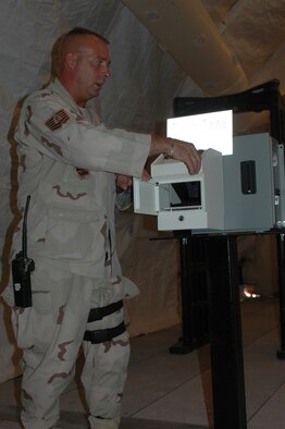 Tech. Sgt. Steve Neith, 379th Expeditionary Security Forces Squadron search pit flight chief, demonstrates how a handprint scanner will work once the new Defense Biometric Identification Database System is complete. 