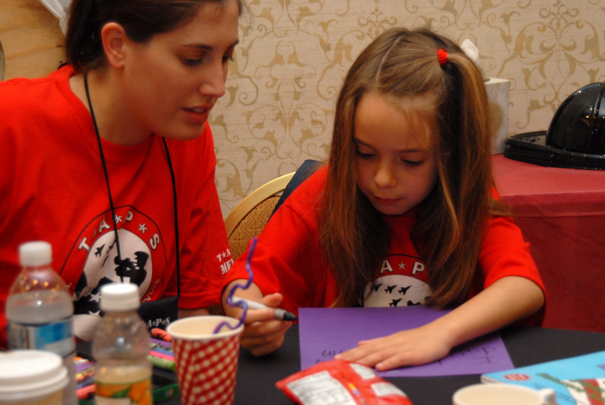Air National Guard Tech. Sgt. Sam Clarke works with 6-year-old Laura Hilton while she writes a letter to her mom and dad during the Tragedy Assistance Program for Survivors camp May 25 at Crystal City, Va. Held over Memorial Day weekend, TAPS was a three-day camp children and family members who have lost a loved one in military service attended that aims to help teach families how to grieve, as well as share their stories and make friends who share their loss. (U.S. Air Force photo/Staff Sgt. Madelyn Waychoff)