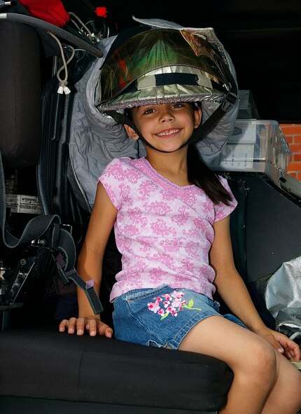 Alexis Patel, 7, RAF Lakenheath family member, tries on a firefighter's helmet while sitting in a firetruck at the bike rodeo June 2 at the RFA Mildenhall BXtra. (U.S. Air Force photo by Karen Abeyasekere)