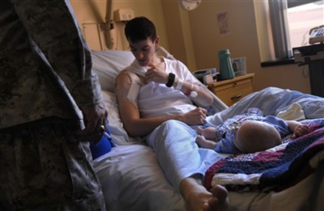 U.S. Army Sgt. Johnson sits on his hospital bed with his 3-month-old son at Tripler Army Medical Center, Hawaii, June 5, 2007, as he shows Chairman of the Joint Chiefs of Staff U.S. Marine Gen. Peter Pace the injuries he sustained while on patrol in Iraq.