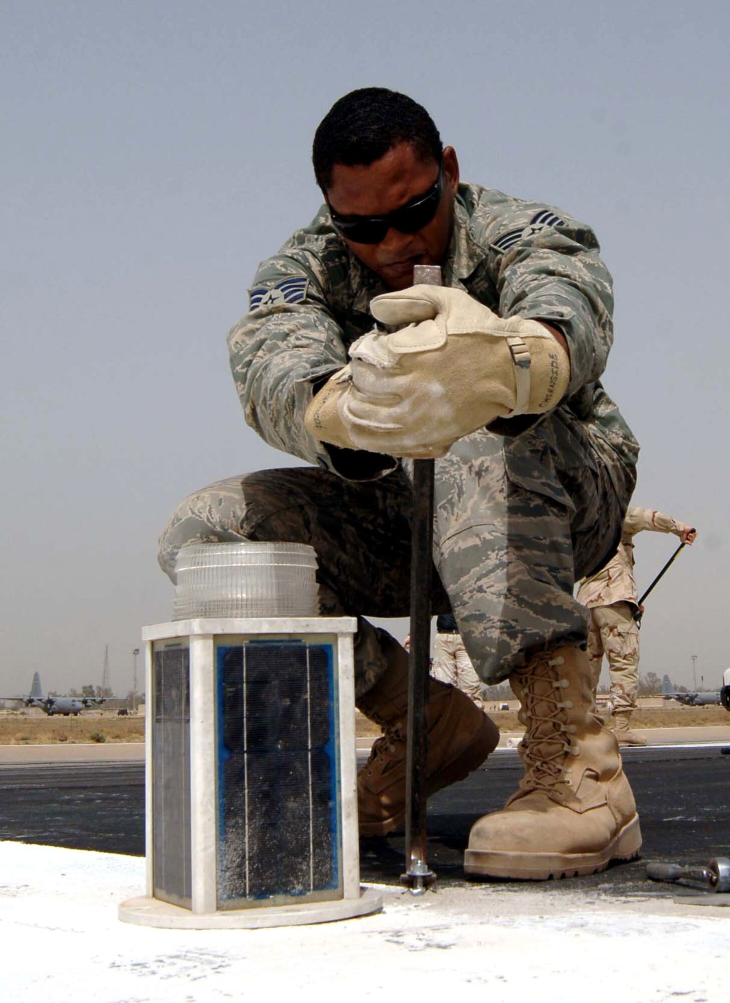 Staff Sgt. Charles Thompson pries up a stripped mounting bolt for a threshold light on the Baghdad International Airport runway May 30 in Iraq. These threshold lights are being installed temporarily to shorten the runway by 3,000 feet so repairs can be made. Sergeant Thompson is a 447th Expeditionary Civil Engineer Squadron electrician. (U.S. Air Force photo/Tech. Sgt. Russell Wicke)
