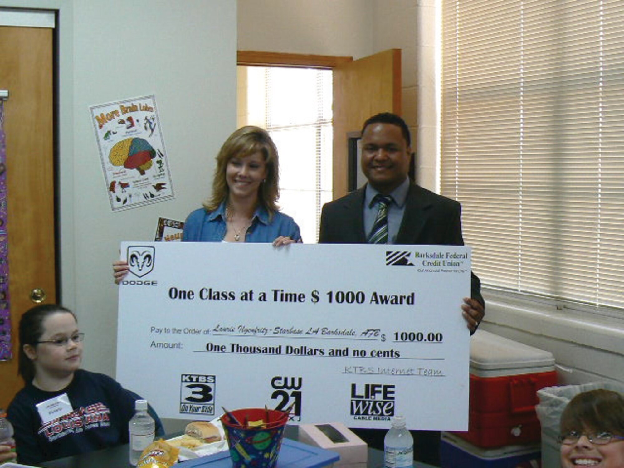 Mrs. Laurie Ilgenfritz, deputy STARBASE director and recipient of the $1000 Landers Dodge, Barksdale Federal Credit Union,  Life Wise Cable Media, KTBS  “One Class at a Time” award, poses with her large check along with KTBS employee, Will Moses. (U.S. Air Force courtesy photo)