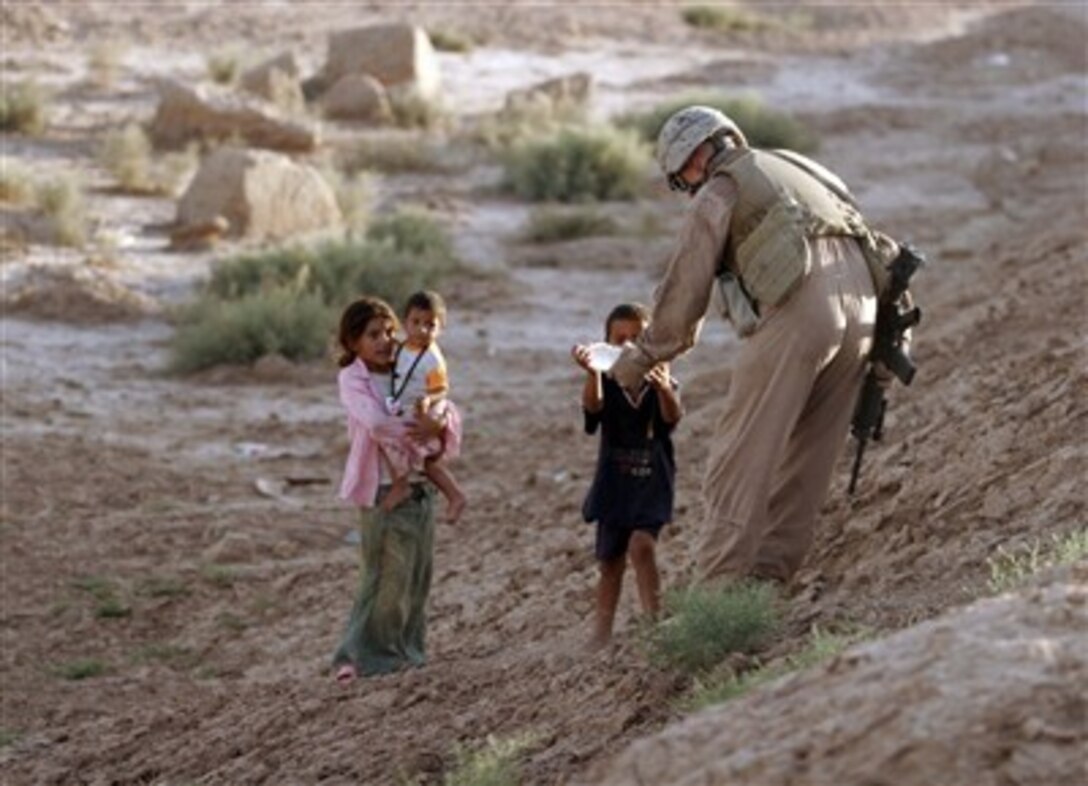 U.S. Marine Corps Cpl. Kyle Harper, a truck leader with Military Police Company, 2nd Maintenance Battalion, hands a bottle of water to an Iraqi child in Al Qam, Iraq, June 5, 2007.