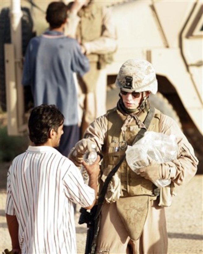 U.S. Marine Corps Cpl. Kyle Harper hands a bottle of water to an Iraqi man on a bridge in Al Qam, Iraq, on June 5, 2007.  Harper is assigned as a truck leader with Military Police Company, 2nd Maintenance Battalion.  