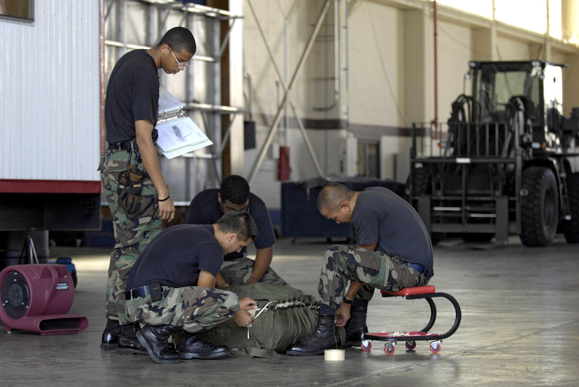 Airman 1st Class Darrius Armstead watches over his team as they pack a parachute in a hangar at Hickam Air Force Base, Hawaii, June 11. They are preparing the parachute to be rigged to a practice airdrop bundle.  The Airmen are from the 15th Logistics Readiness Squadron Combat Mobility Element.  (U.S. Air Force photo/Tech. Sgt. Shane A. Cuomo) 