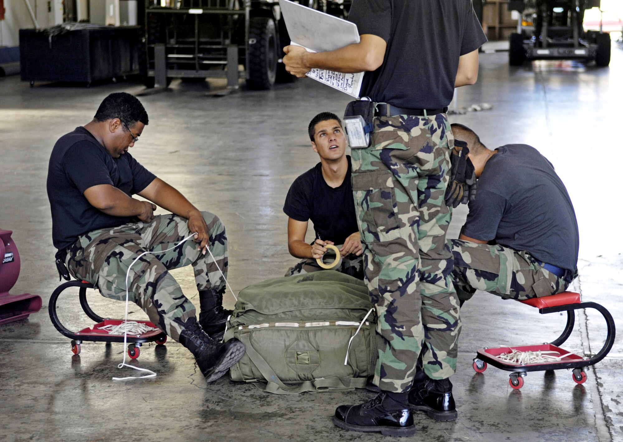 Airman 1st Class Darrius Armstead watches over his team as they pack a parachute in a hangar at Hickam Air Force Base, Hawaii, June 11. They are preparing the parachute to be rigged to a practice airdrop bundle.  The Airmen are from the 15th Logistics Readiness Squadron Combat Mobility Element.  (U.S. Air Force photo/Tech. Sgt. Shane A. Cuomo) 