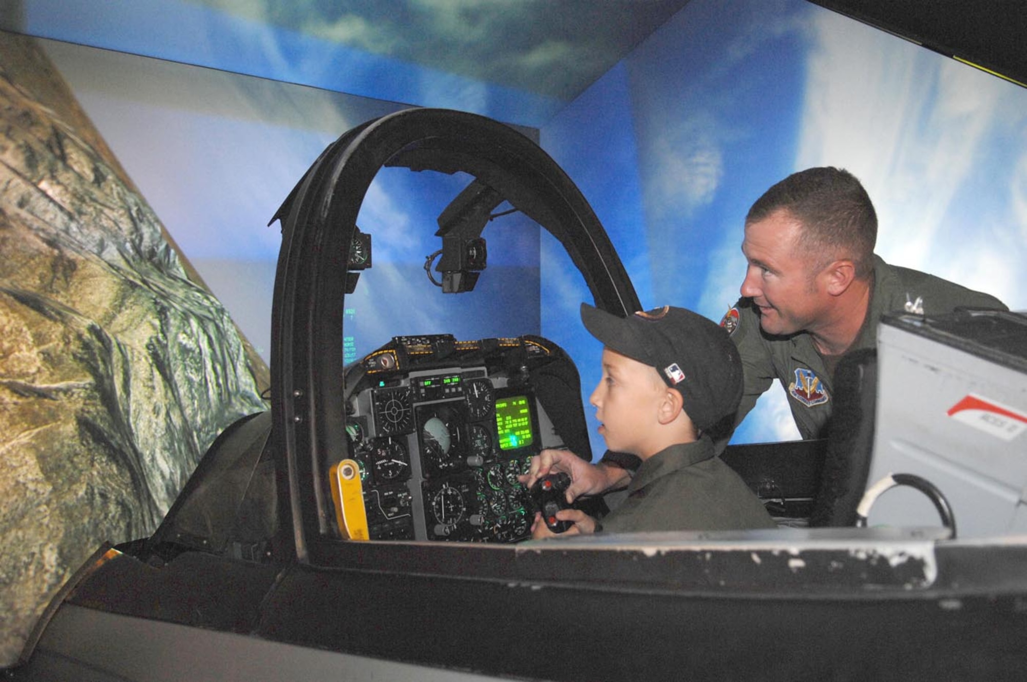 Capt. Benjamin Fallin, a pilot for the 358th Fighter Squadron here, helps "Pilot for a Day" Matthew Belleau, 7, perform a roll maneuver in an A-10 flight simulator here. After stepping out of the simulator, Matthew found it difficult to contain his excitement, jumping up and down and saying, “That was fun!” (U.S. Air Force photo/Airman 1st Class Alesia D. Goosic)