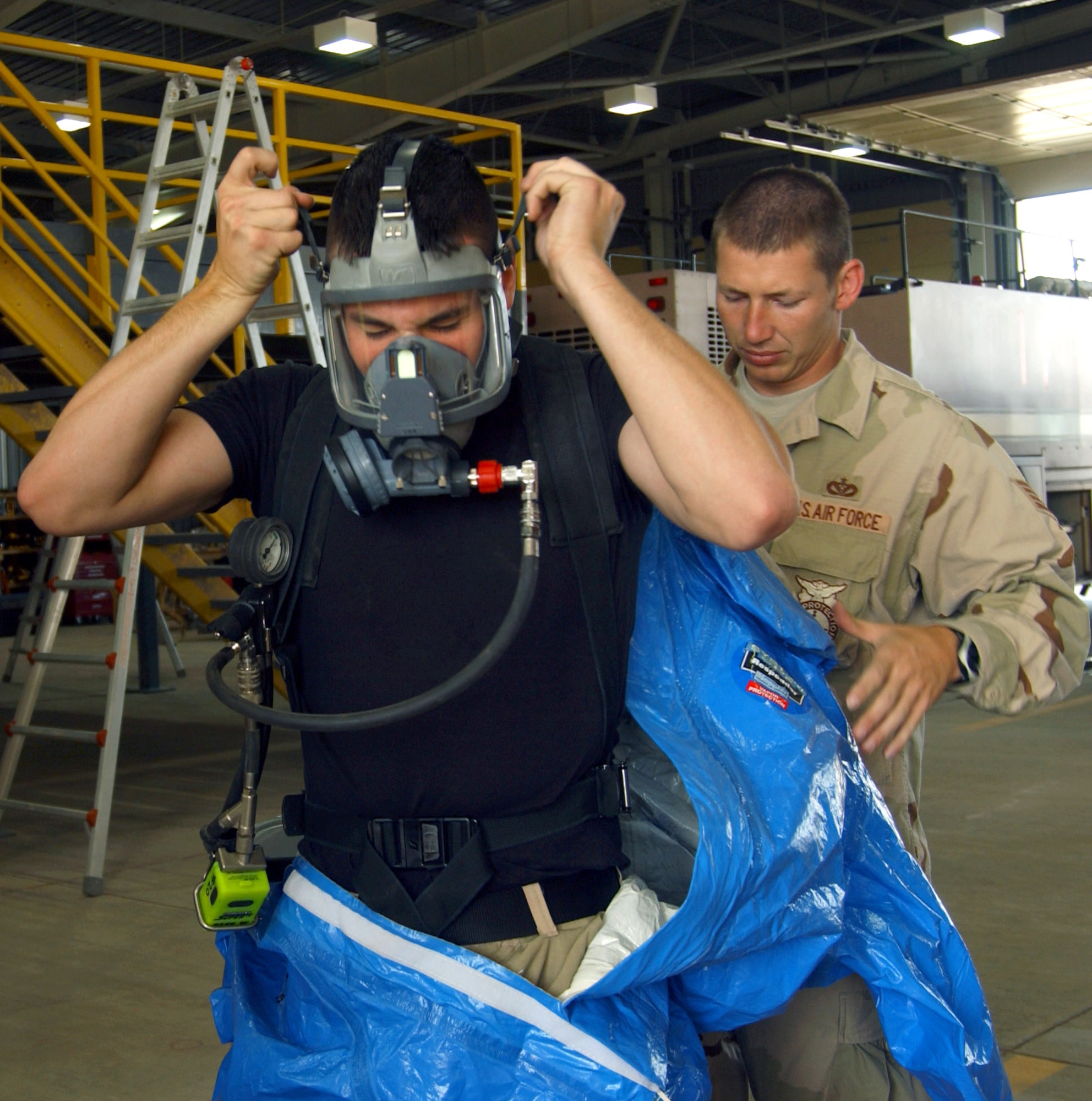 Staff Sgt. Ryan Roxburgh helps Airman 1st Class Glenn Rodgers put on a blue Level A suit to simulate a chemically contaminated firefighter during a training exercise June 5 at Balad Air Base, Iraq. The firefighters set up a hazardous-material decontamination line and practiced so that they would be able to quickly respond to any real-world threat within 10 minutes. The Airmen are firefighters with the 332nd Expeditionary Civil Engineer Squadron Fire and Emergency Services Flight.  (U.S. Air Force photo/1st Lt. Shannon Collins)