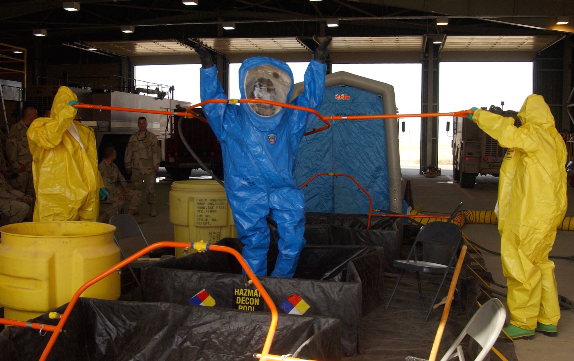 Army Spc. Michael Harms (left) and Airman 1st Class Jace Correa, in yellow Level B suits, raise and lower a decontamination shower ring as Airman 1st Class Glenn Rodgers, in a blue Level A suit, simulates a contaminated firefighter during a training exercise June 5 at Balad Air Base, Iraq. The firefighters set up a hazardous-material decontamination line and practiced so that they would be able to quickly respond to any real-world threat within 10 minutes. The servicemembers are firefighters with the 332nd Expeditionary Civil Engineer Squadron Fire and Emergency Services Flight. (U.S. Air Force photo/1st Lt. Shannon Collins)