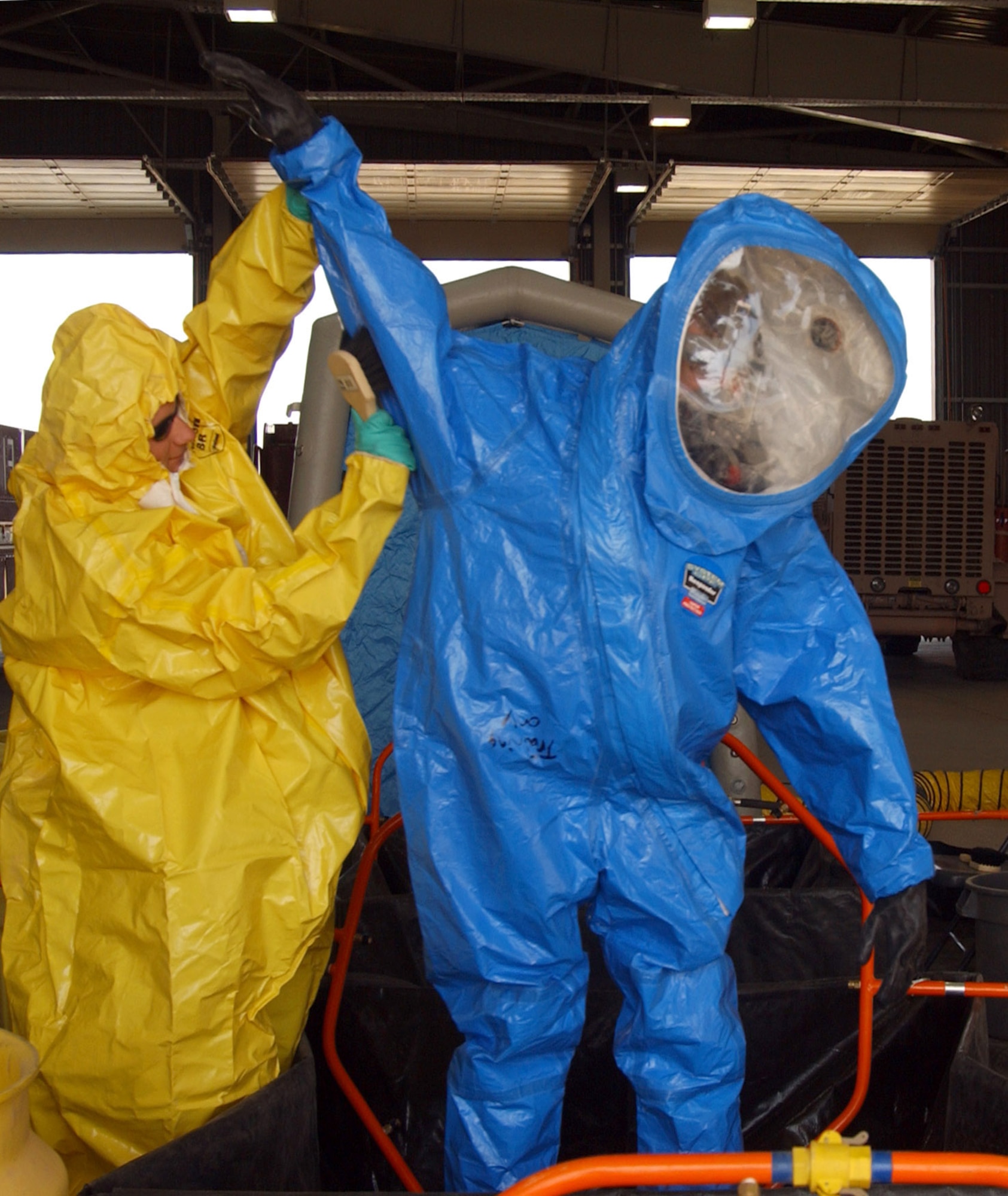 While wearing a yellow Level B suit, Army Spc. Michael Harms simulates scrubbing chemicals off of Airman 1st Class Glenn Rodgers, in a blue Level A suit, during a training exercise June 5 at Balad Air Base, Iraq. The firefighters set up a hazardous-material decontamination line and practiced so that they would be able to quickly respond to any real-world threat within 10 minutes. The servicemembers are firefighters with the 332nd Expeditionary Civil Engineer Squadron Fire and Emergency Services Flight. (U.S. Air Force photo/1st Lt. Shannon Collins)