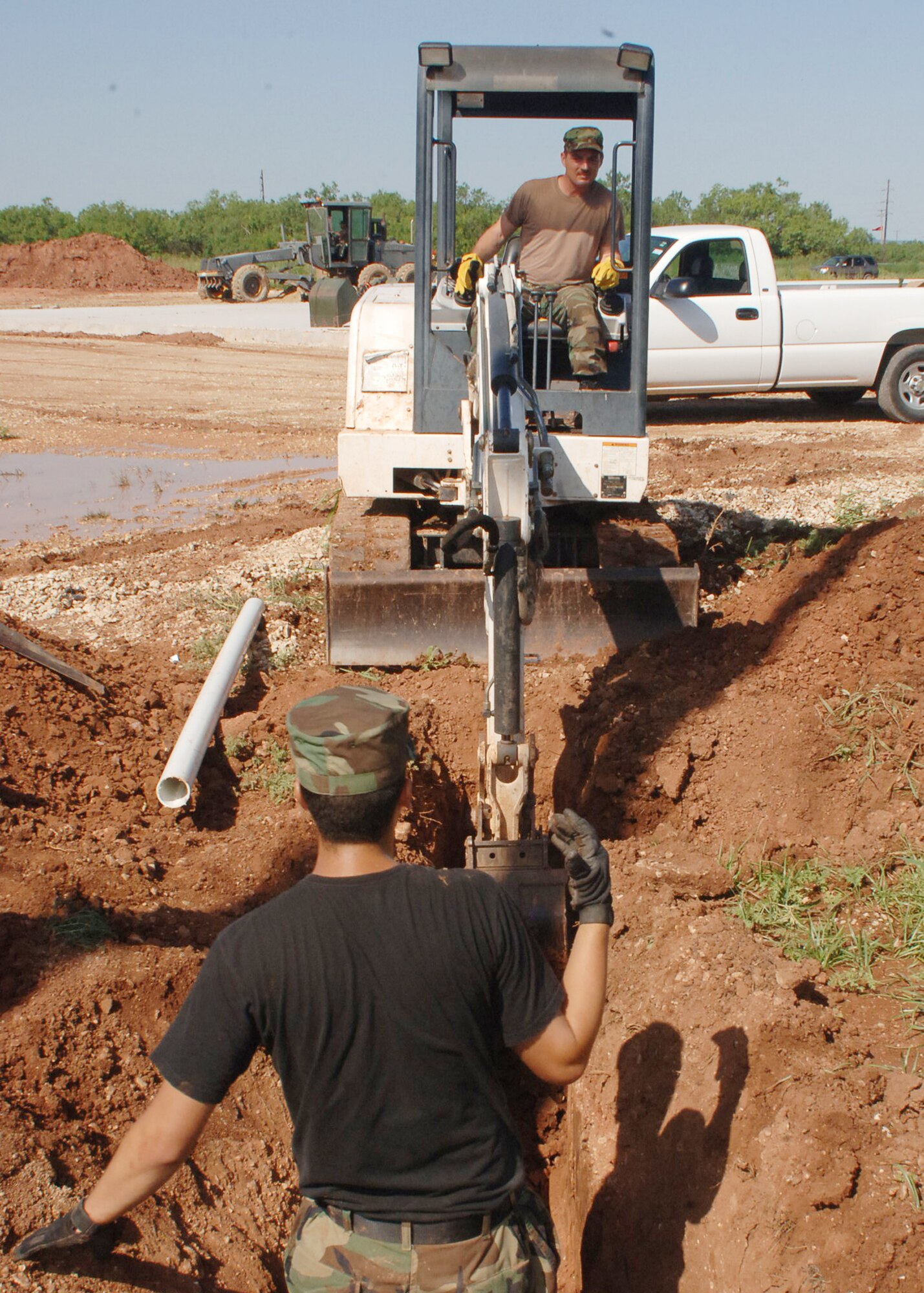 DYESS AIR FORCE BASE, Texas -- Airman Victor Aldana indicates how far forward Tech. Sgt. Matthew Cross, 7th Civil Engineer Squadron, can drive a Bobcat tractor June 14. They are digging a hole for a water line to be put in near the cantonment area for Operational Readiness Exercises. (U.S Air Force photo by Airman 1st Class Felicia Juenke)