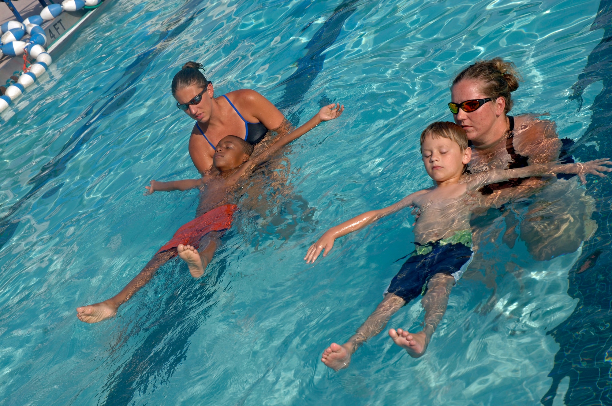 Allison Fleifchauer, head lifeguard and swim instructor, supports C.J. Belton, 6, (left) and Tiffany Taylor, lifeguard and swim instructor, supports Trey Shiflett, 6, (right) and teaches them to relax and allow their bodies to float at the base pool June 12.  (U.S. Air Force photo/ Staff Sgt. April Quintanilla) 