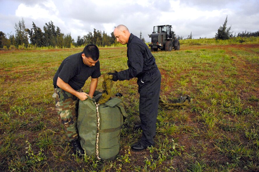 Airman 1st Class Justin Stevens and Tech. Sgt. Brian Snow collect a parachute from a practice airdrop bundle after being drop by a C-17 Globemaster III June 11 at the Kahuku Training Range in Hawaii. The C-17s, from the 535th Airlift Squadron at Hickam Air Force Base, are conducting their quarterly airdrop qualifications. The Airmen are air transportation specialist from the 15th Logistics Readiness Squadron Combat Mobility Element. (U.S. Air Force photo/ Tech. Sgt. Shane A. Cuomo)