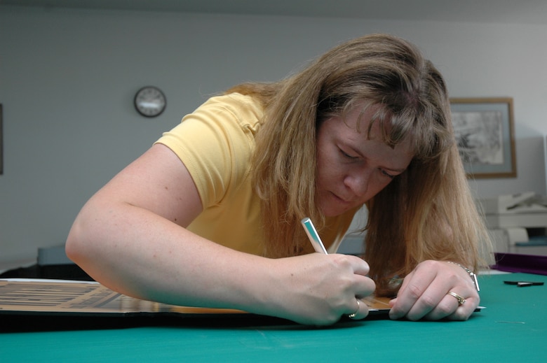 Brook Gerard carefully trims excess material from a vacation bible school poster for the base chapel. She is an illustrator and video-teleconferencing manager at the base multi-media center. (U.S. Air Force photo / Airman 1st Class Dillon White)