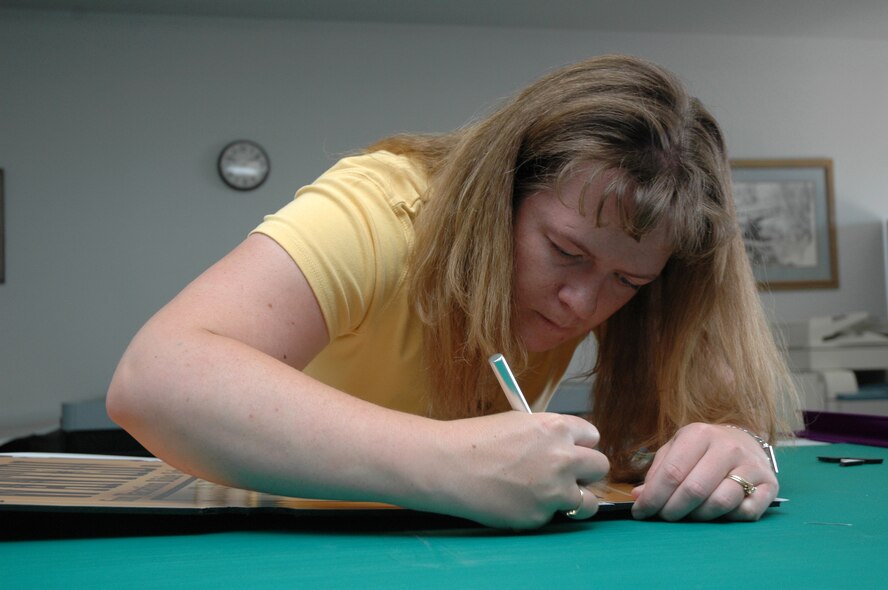Brook Gerard carefully trims excess material from a vacation bible school poster for the base chapel. She is an illustrator and video-teleconferencing manager at the base multi-media center. (U.S. Air Force photo / Airman 1st Class Dillon White)