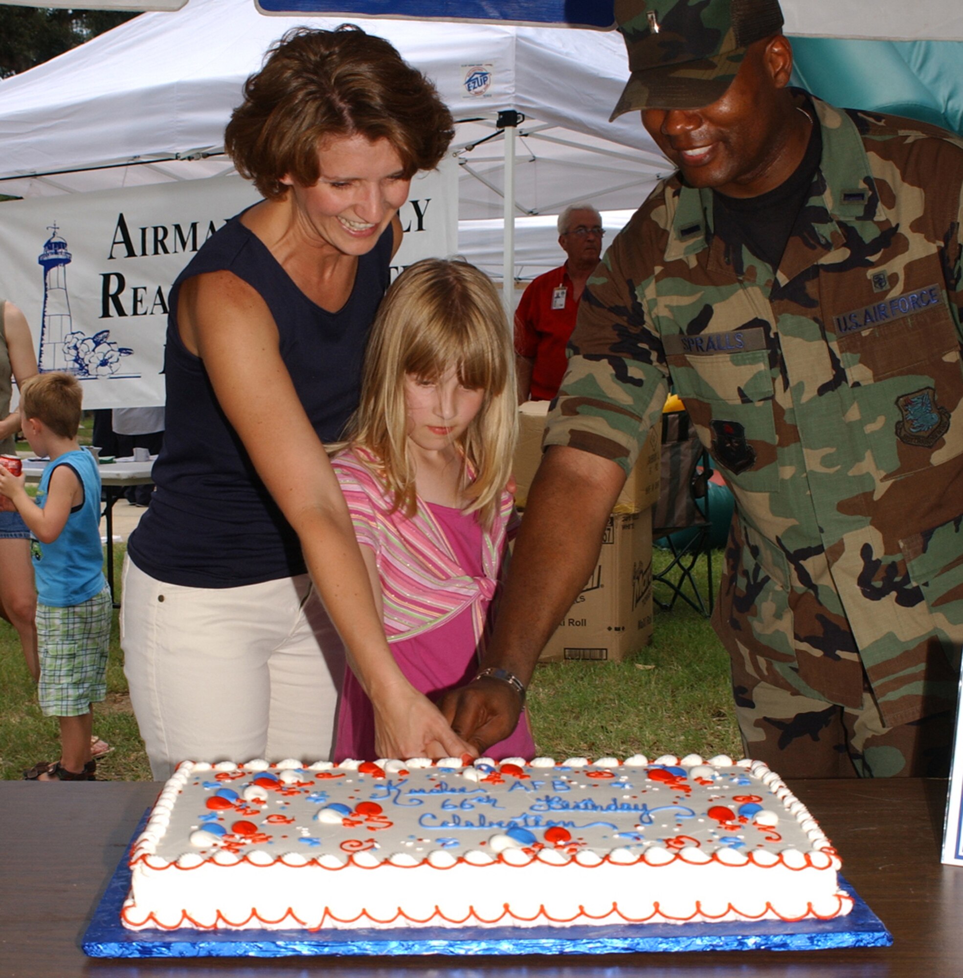 From left, Laura and 8-year-old Claire Capasso  join 1st Lt. Samuel Spralls in cutting the cake at Keesler’s 66th birthday picnic June 14 in marina park.  The Capassos are the wife and daughter of Brig. Gen. Paul Capasso, 81st Training Wing commander.  Lieutenant Spralls, 81st Medical Support Squadron, was project officer for the event, which was hosted by the company grade officers council.  (U. S. Air Froce photo by Kemberly Groue)