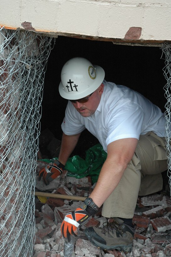 Steve Cassidy, Advanced Explosives Demolition explosives technician, grabs dirt to place in one of the 18 holes drilled to hold the explosives for the demolition of a 95-foot brick chimney June 16. The dirt helps prevent a rifling effect with the explosives. A total of eight pounds of explosives were used to bring down the chimney. (U.S. Air Force photo/Airman Nathan Riley) 