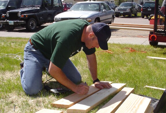 Master Sgt. Randy Glover, 90th Maintenance Operations Squadron, marks a plank of wood to be cut at in a local parking lot May 31. Volunteers from the 90th Maintenance Group made picnic tables for a community service project (Photo by 2nd Lt. Jim Gutierrez).