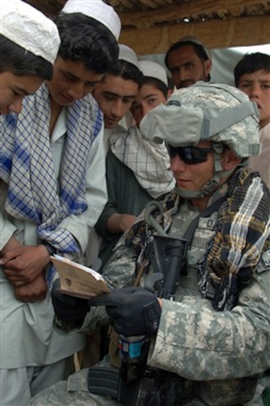 Sgt. Britt Damon points out features in a book as he interacts with local children during a cordon and search conducted with the Afghan National Police in Nani, Afghanistan, on June 3, 2007.  Damon is with the Armyís Human Terrain Team, 4th Brigade Combat Team.  