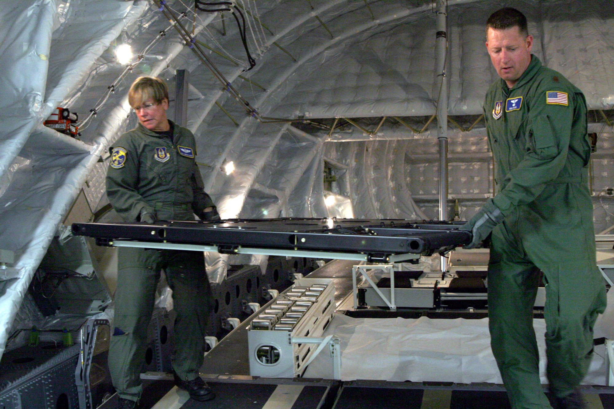 Senior Master Sgt. Jennifer LaPore, C-17 Assistant Loadmaster Superintendent for the 301st AS and Maj. Kenneth Tyler, nurse with the 349th AES, join forces carrying a troop seat component to assemble seating for members of the 939th Services Flight from Portland Air National Guard Base, Ore. who will be boarding and with a destination Mildenhall for their annual tour training. This C-17 Globemaster III flight was the “Heritage Trip” for a team from the  301st  AS, traveling to England with the 89 year old commander of the World War II version of the 301st  AS, the 301st Troop Carrier Squadron. Along with transporting the 939th SVF the 349th AES also utilized the flight for training in assembling patient litters, patient movement and treatment, and practicing loading a patient during “engine running” conditions. (U.S. Air Force photo by Master Sgt. Wendy Weidenhamer)
