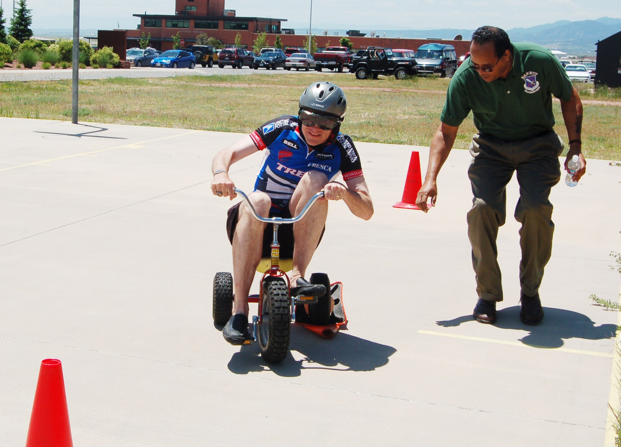 Col. Jay G. Santee, 21st Space Wing commander, struggles to maneuver around a cone while riding a tricycle and wearing "drunk" goggles on Sports and Field Day June 14. The goggles are meant to show how drinking can affect the ability to drive. Colonel Santee's team lost the trike race to the Director of Staff team. (U.S. Air Force photo by Corey Dahl)