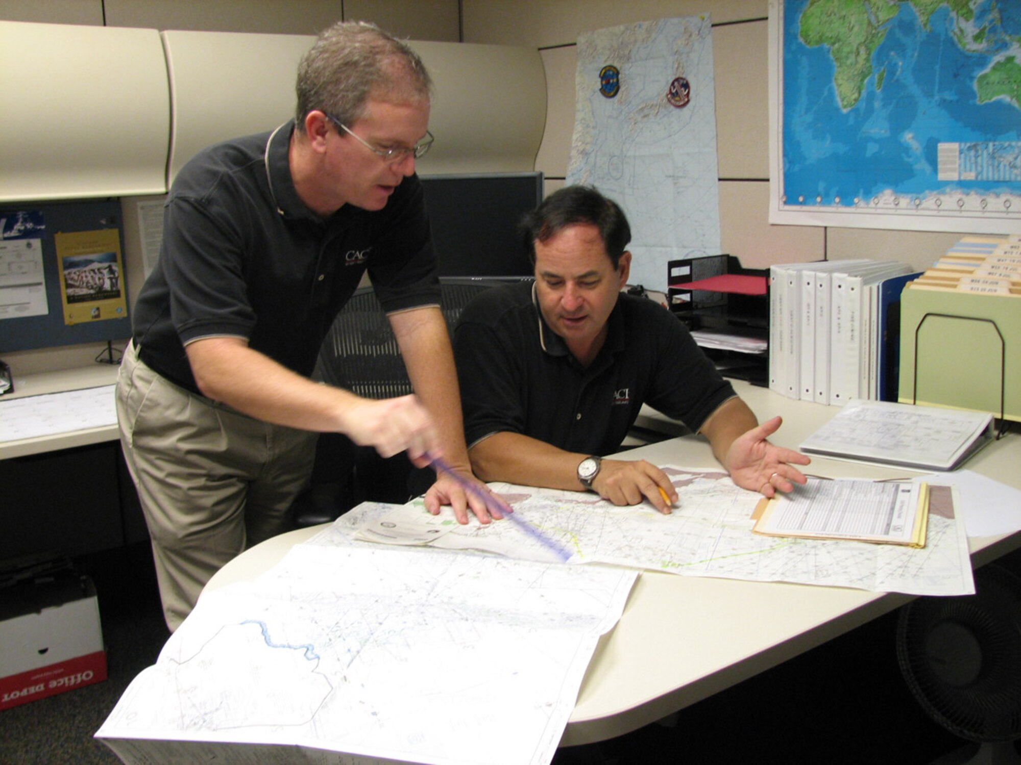 Jeff Frye, primary Air Force executive airlift support planner, and Mark Piscioneri, primary Navy executive airlift planner, plan an executive airlift mission in the Pacific theater.  Both are CACI International, Inc., contract employees working for the 613th Air and Space Operations Center Air Mobility Division. CACI has provided Pacific Air Force’s mobility aircraft planning and dispatch functions for six years, but this is the first time a civilian contractor will perform these services for Commander, Pacific Fleet’s Executive Transport Detachment. (USAF Photo by Capt. Yvonne Levardi.)