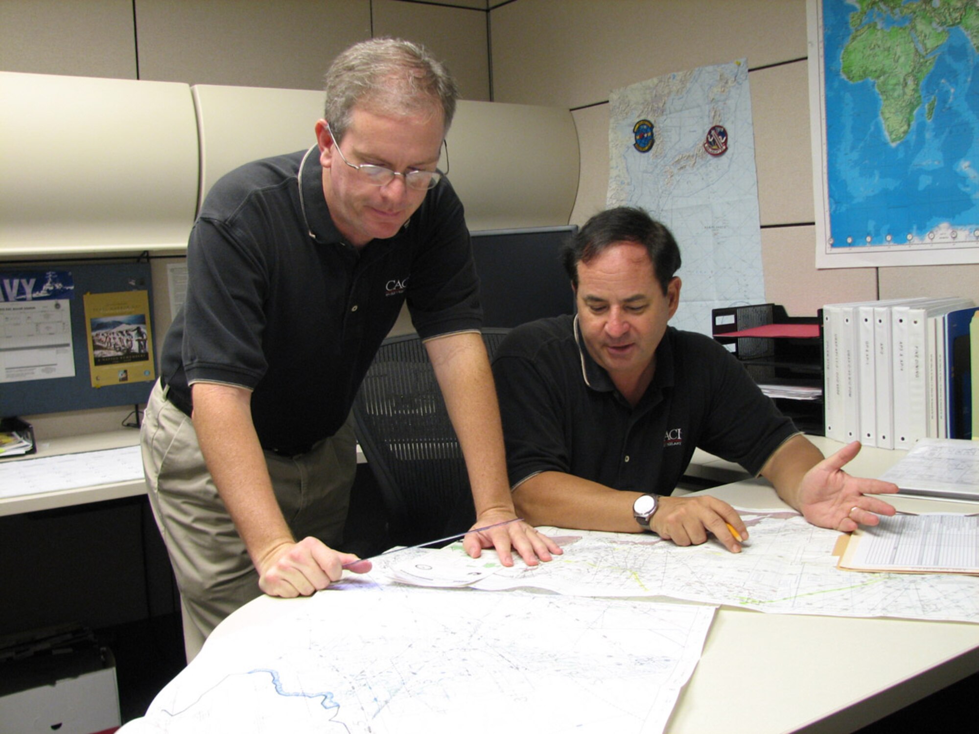 Jeff Frye, primary Air Force executive airlift support planner, and Mark Piscioneri, primary Navy executive airlift planner, plan an executive airlift mission in the Pacific theater.  Both are CACI International, Inc., contract employees working for the 613th Air and Space Operations Center Air Mobility Division. CACI has provided Pacific Air Force’s mobility aircraft planning and dispatch functions for six years, but this is the first time a civilian contractor will perform these services for Commander, Pacific Fleet’s Executive Transport Detachment. (USAF Photo by Capt. Yvonne Levardi.)