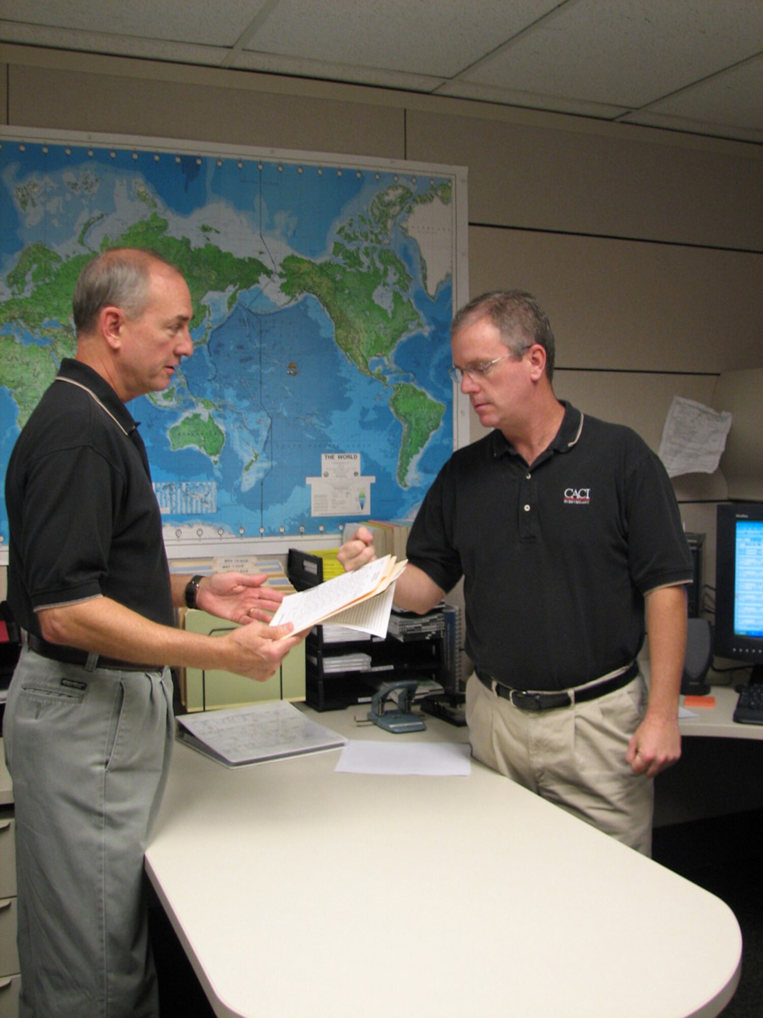 Ed Salisbury, task lead, executive airlift support and operational support airlift, 613th Air and Space Operations Center Air Mobility Division, discusses an upcoming executive airlift mission with Jeff Frye, primary Air Force executive airlift support planner. Both are CACI International, Inc., contract employees.  CACI has provided Pacific Air Force’s mobility aircraft planning and dispatch functions for six years, but this is the first time a civilian contractor will perform these services for Commander, Pacific Fleet’s Executive Transport Detachment. (USAF Photo by Capt. Yvonne Levardi.)