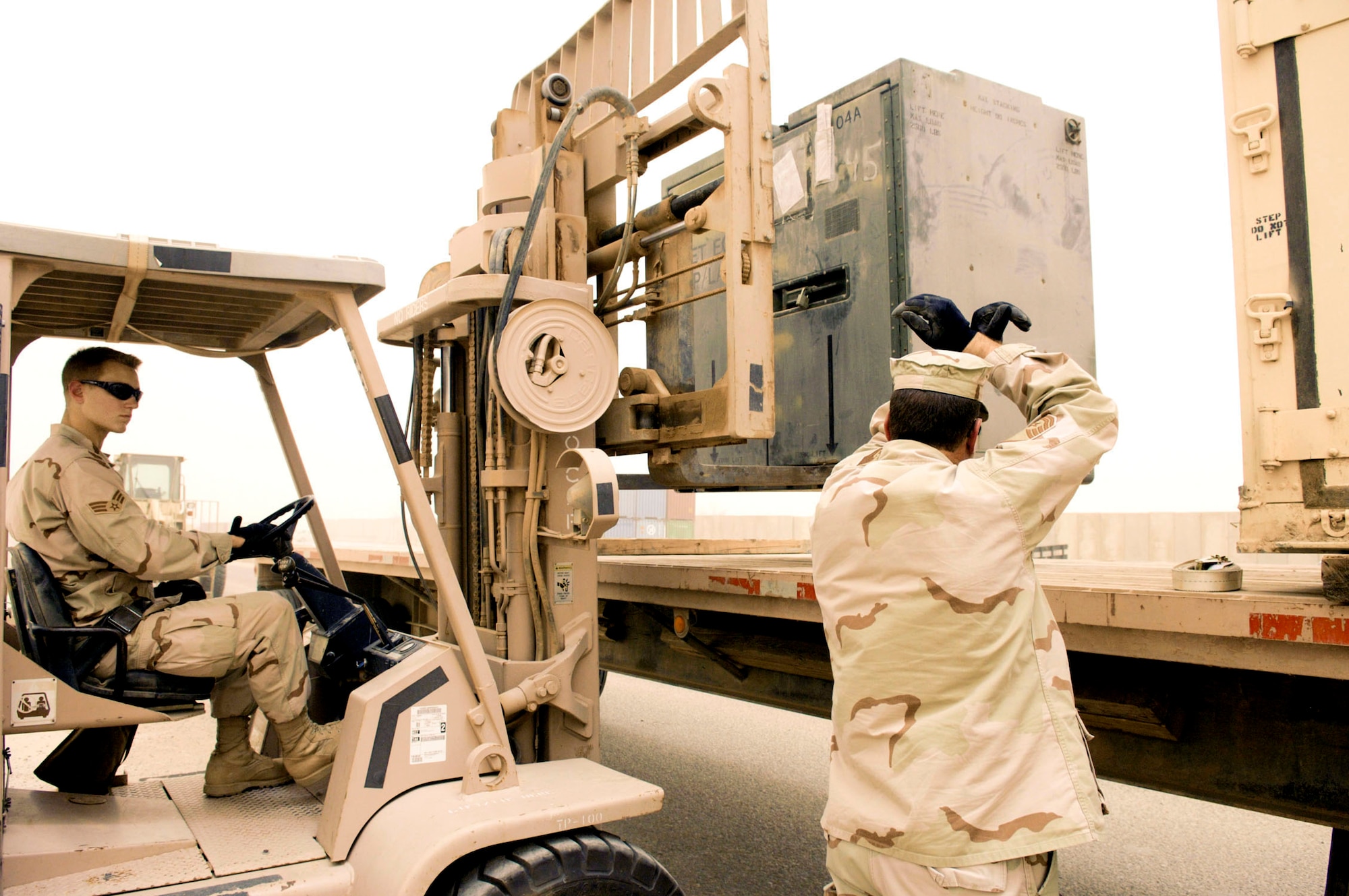 Enduring heavy dust and winds, Master Sgt. Steven Anderson directs Senior Airman Christopher Kieffer into position to place a container full of M-16's onto a trailer during a base-wide arming exercise June 14 at Ali Air Base, Iraq. Both are members of the 407th Expeditionary Logistics Readiness Squadron. Ali AB Airmen participated in the exercise to help fine-tune weapons distributing procedures in case of a real-world threat to the base. (U.S. Air Force photo/Master Sgt. Robert W. Valenca) 
