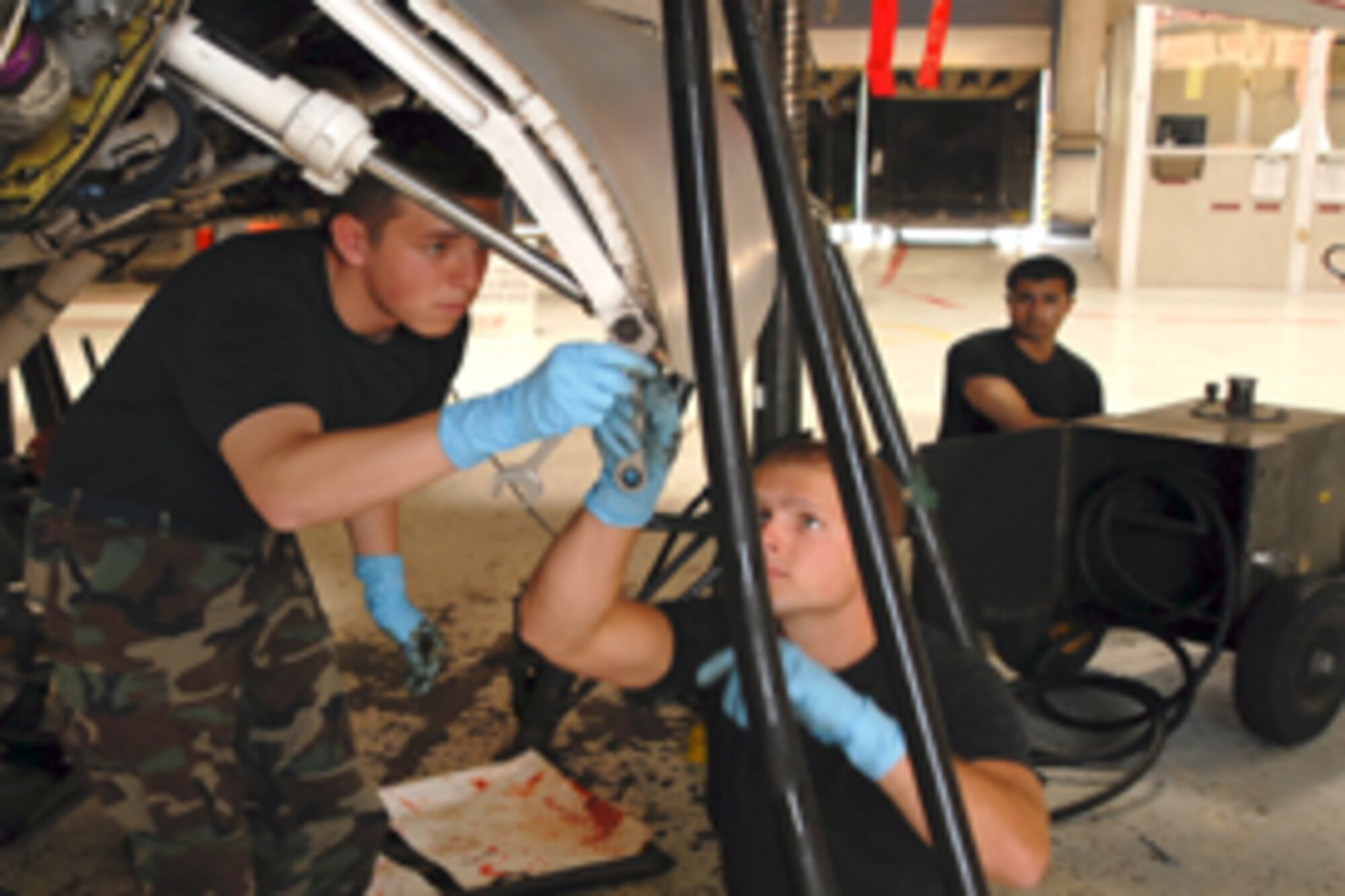 FROM LEFT: Cadets 2nd Class Tim Green and Joe Miller remove a bolt to release the landing gear door on an F-16 Monday after Cadet 2nd Class Sid Maru jacks up the landing gear. The U.S. Air Force Academy cadets are at Luke participating in the
Operation Air Force Third Lieutenant course this summer. Photo by Airman 1st Class Christopher Hatch.