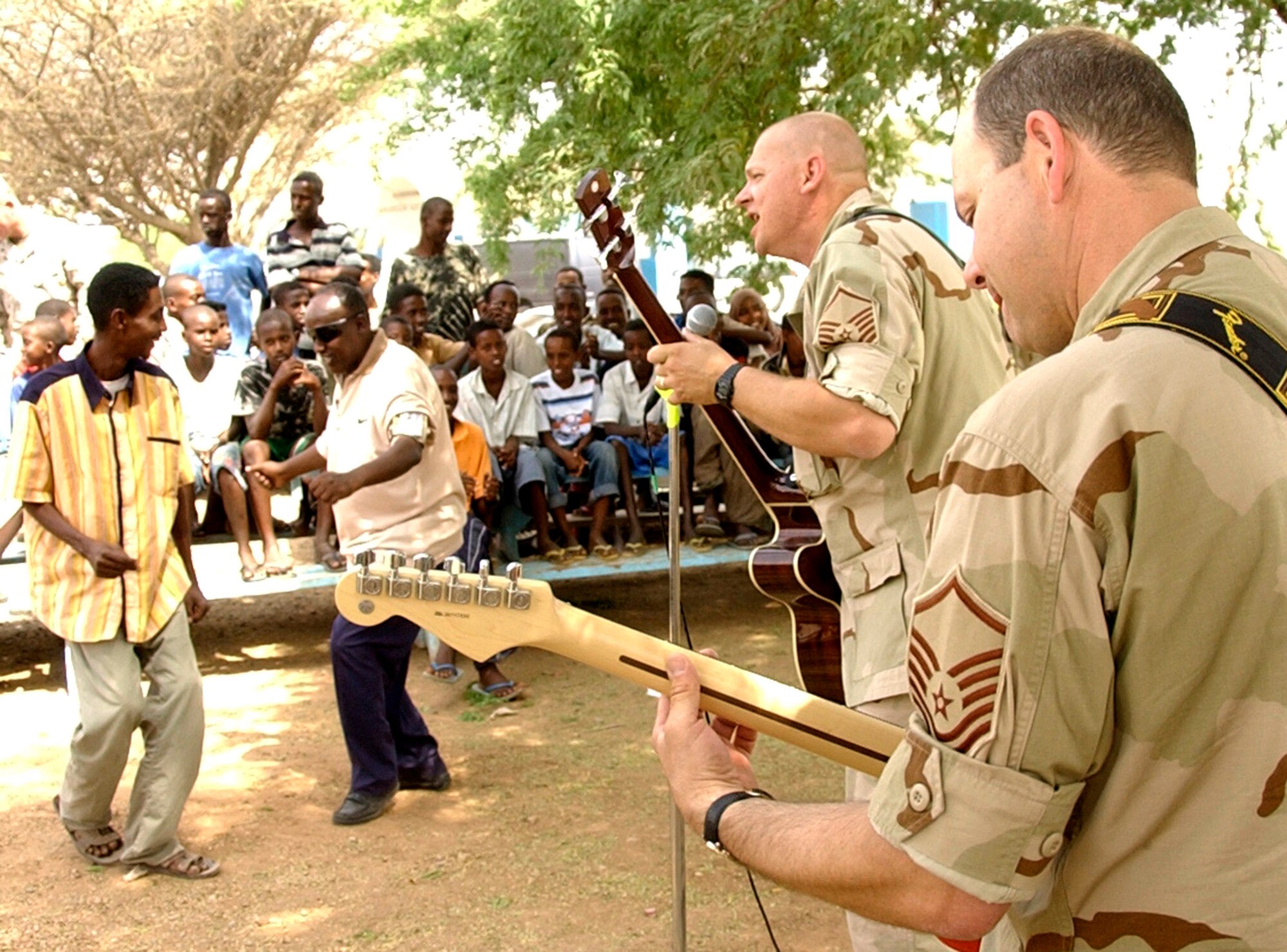 Master Sgt. Bill Swanberg sings to the crowd while Master Sgt. Greg Koger backs him up on guitar during "Thunder Roll's" outreach concert in Douda village June 20. This was the first time a band had ever played in the village, located five miles from Camp Lemonier, Djibouti. Sergeant Swanberg is the bassist and Sergeant Koger is lead guitarist with the U.S. Central Air Forces expeditionary band "Thunder Roll." (U.S. Air Force photo/Staff Sgt. Samuel King Jr.) 