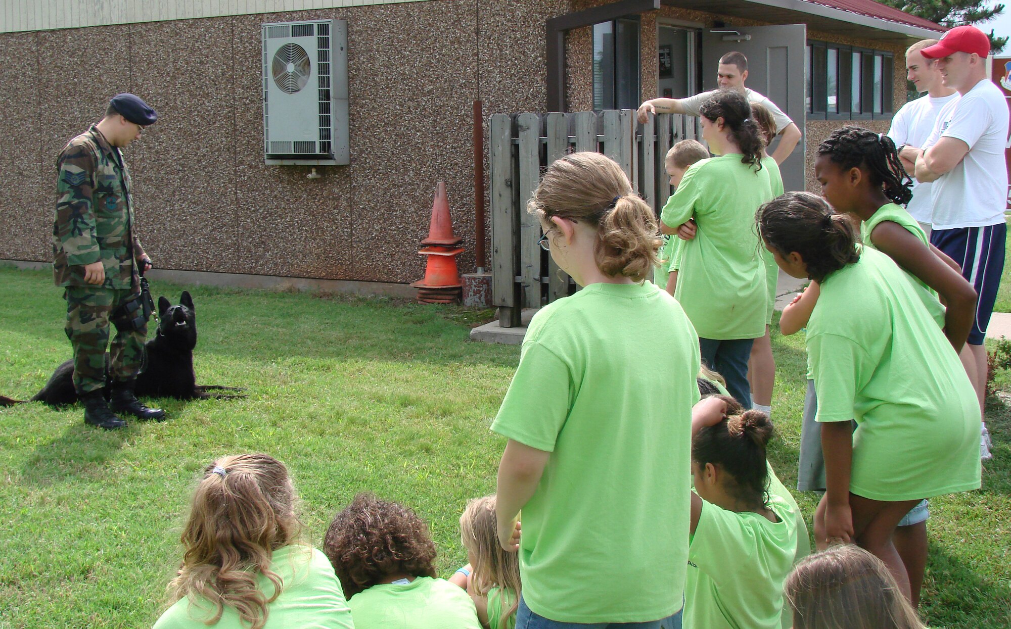 Military working dog Sinne waits for instruction from SSgt. Andrew O'Dell of the 71st Security Forces Squadron, while children and counselors from Camp Tomahawk look on.