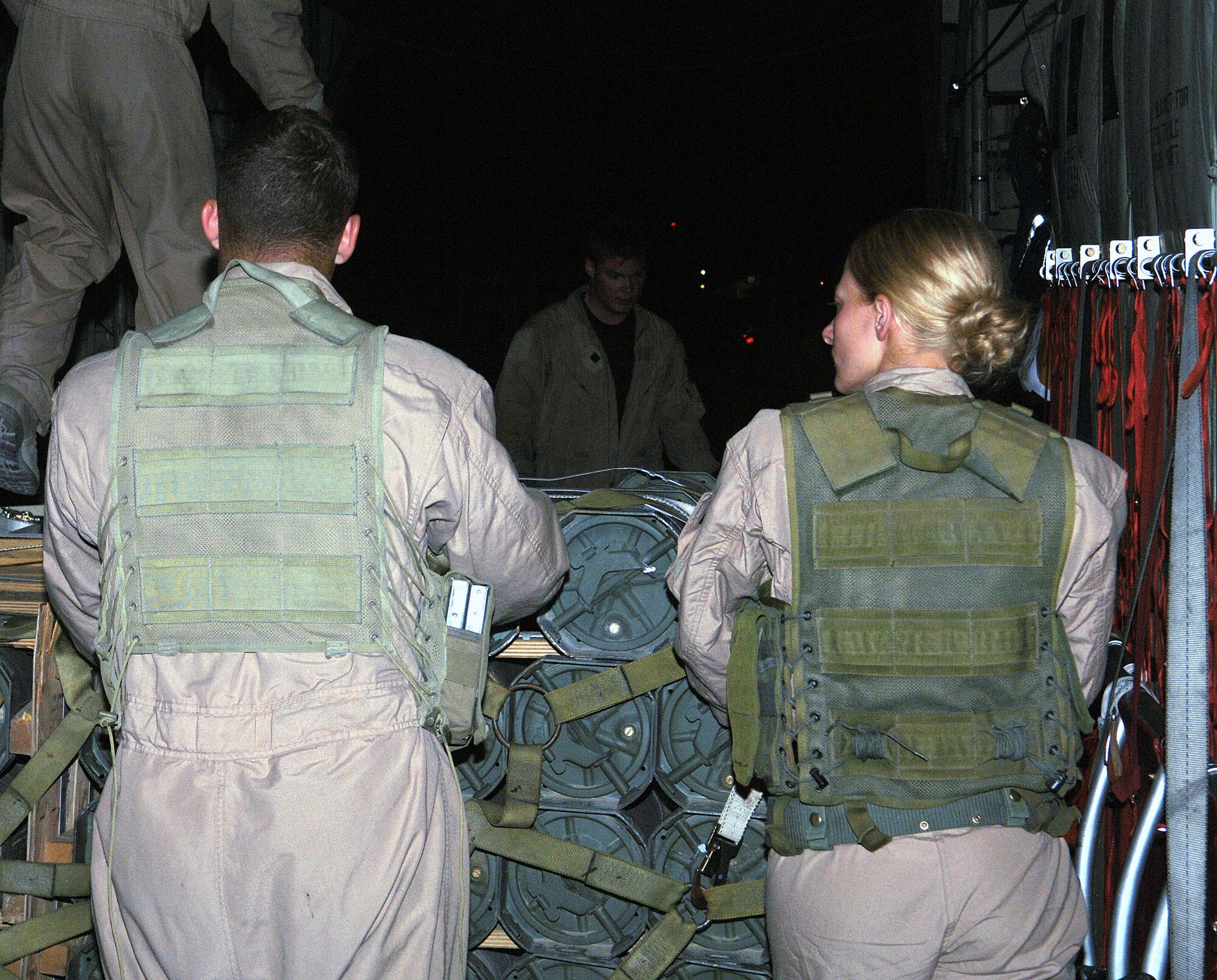Senior Airman Michael Madden (left) and Airman 1st Class Bobbie Ohm, 455th Expeditionary Security Forces Squadron Fly Away Security Team members, assist a C-130 crew unloading palletes at the end of their mission. Airman Madden and Airman Ohm are deployed from Ramstein Air Base, Germany. (photo by Capt. Nora Eyle)