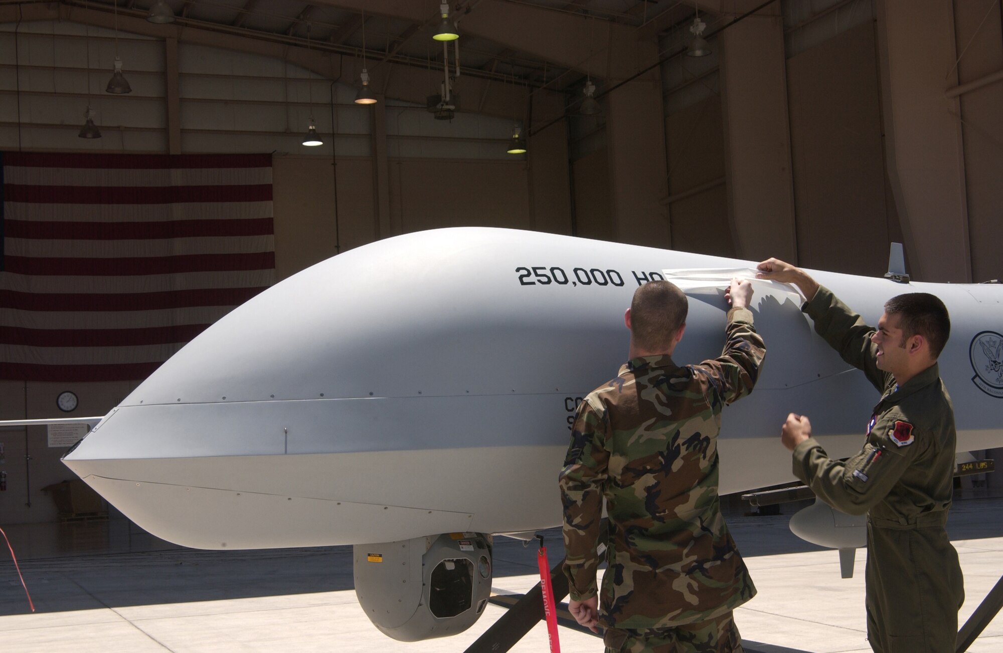 Airman 1st Class Jason Allen (left), 432nd Aircraft Maintenance Squadron integrated avionics specialists, and Senior Airman Chris Ayers, an MQ-1 sensor operator assigned to the 11th Reconnaissance Squadron, revealed the 250,000th flight hour milestone imprinted on the MQ-1 Predator airframe June 22, 2007, at Creech Air Force Base, Nev. (U.S Air Force Photo by Senior Airman Larry E. Reid Jr.)   