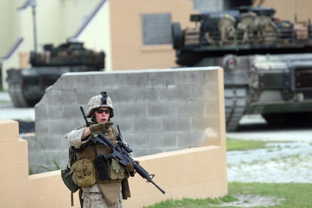 A Marine with Company K, 3rd Battalion, 2nd Marine Regiment, 2nd Marine Division, directs his squad while patrolling alongside M1A1 Abrams Tanks through the Military Operations in Urban Terrain training facility during a ten-day training evolution called Exercise Practical Bastard, June 18-27. The training also included marksmanship, improvised explosive device detection, the Motorized Operations Training Package and working alongside Assault Amphibian Vehicles.