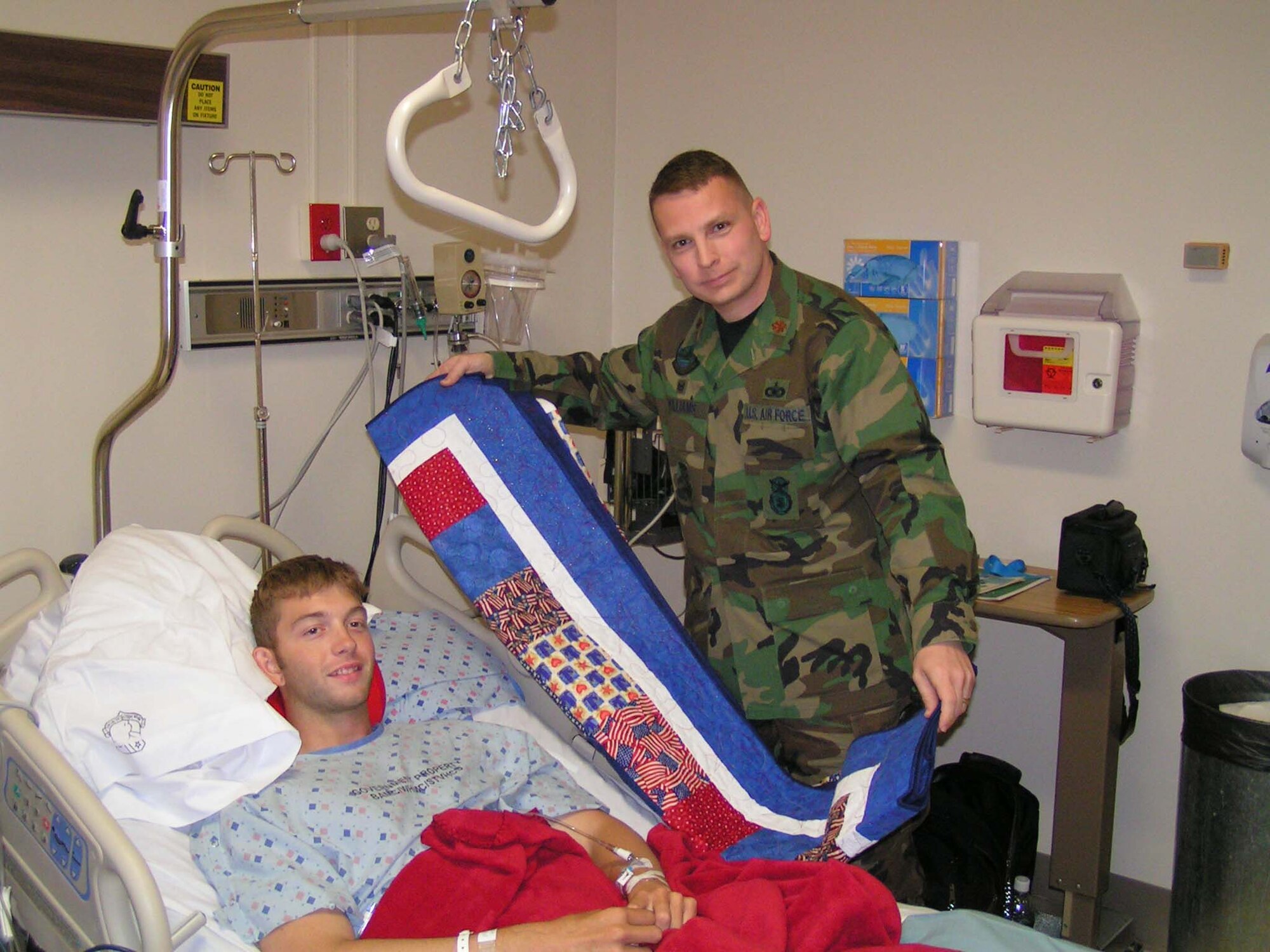 Maj. David Williams, 90th Security Support Squadron commander, presents a quilt made by his wife, Jennifer, to Senior Airman Joshua Brooks, 90th SSPTS, who was injured in Iraq. The mission of the Quilts of Valor foundation is to cover all combat wounded and injured service members from the war on terror (Photo by Master Sgt. Shawn Matzen). 

