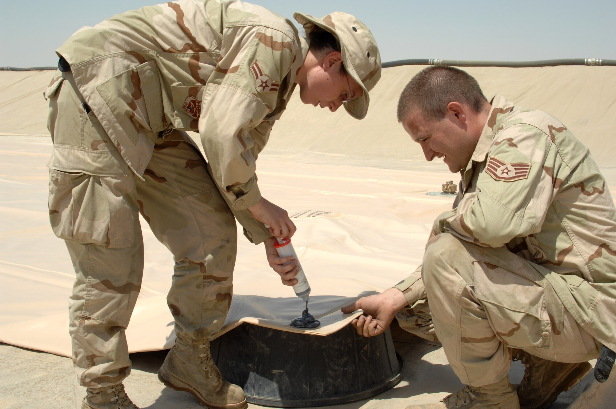 Airman 1st Class Sarah Sarten and Staff Sgt. Mark Chance seal the corners of a new fuel bladder June 19 at Kirkuk Regional Air Base, Iraq. The bladder will be filled with JP-8 jet fuel.  Fuel storage bladders are collapsible, flexible storage containers that provide temporary as well as long term fuel storage.  Airman Sarten and Sergeant Chance are with the 506th Expeditionary Logistics Readiness Squadron.  (U.S. Air Force photo/Senior Airman Kristin Ruleau)