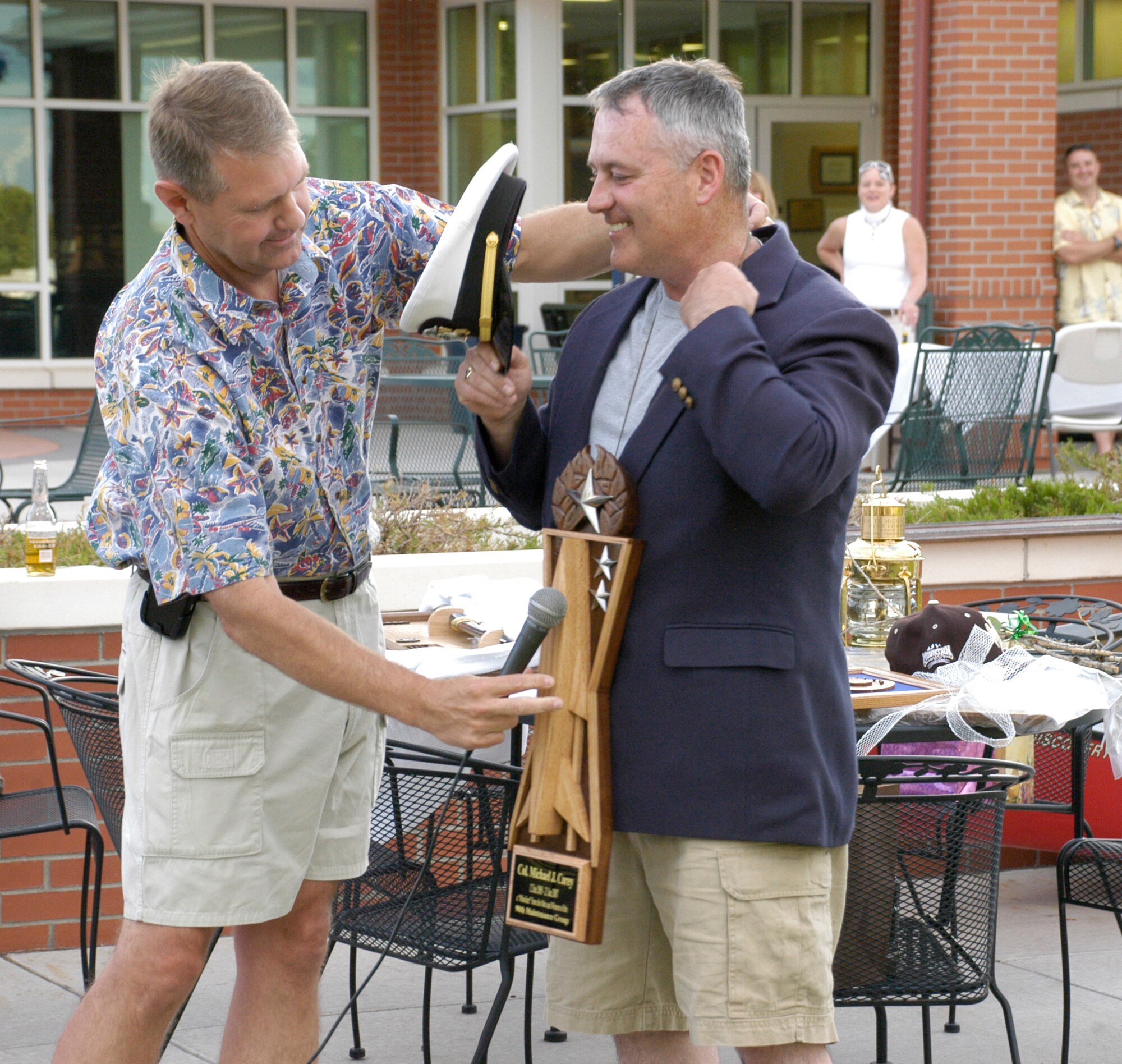 Col. L.B. Mobley, 90th Maintenance Group commander, presents Col. Mike Carey, 90th Space Wing commander, his going-away gift at the Colonel and Mrs. Carey’s farewell party at the golf course June 15. The gift was a wooden pocket rocket badge in honor of Colonel Carey’s support to the 90th MXG over the past two years (Photo by 2nd Lt. Lisa Meiman).