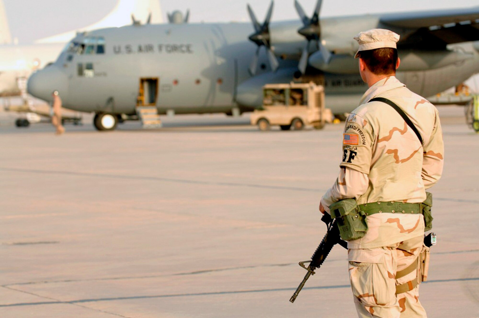 Airman 1st Class Morgan Constantino looks on as a C-130 Hercules crew begins their pre-flight inspection June 22 at Ali Air Base, Iraq.  Airman Constantino, a member of the 407th Expeditionary Security Forces Squadron, is assigned to flightline defense, protecting U.S. and coalition assets from insurgent intelligence gathering efforts and attacks. (U.S. Air Force photo/Master Sgt. Robert W. Valenca)