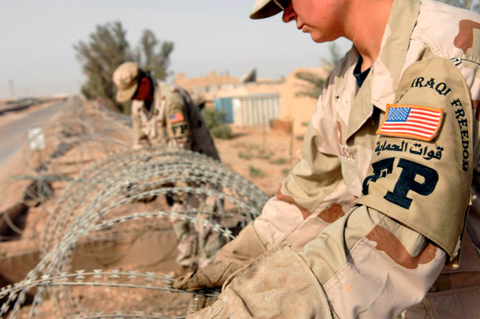Tech. Sgt. Hunter Lescoe (left) and Senior Airman Margaret Wilson unwind concertina wire they are installing on a wall to protect the 407th Expeditionary Communication Squadron compound on Ali Air Base, Iraq. Both are members of the 407th Expeditionary Security Forces Squadron.  (U.S. Air Force photo/Master Sgt. Robert W. Valenca)