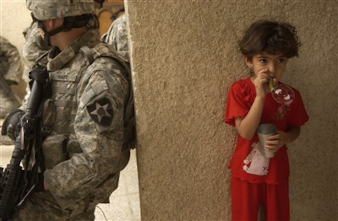 An Iraqi girl blows bubbles while U.S. Army soldiers keep an eye on the street outside of her house during a cordon and search in the Rashid district of Baghdad, Iraq, on June 20, 2007.  The soldiers are with the 1st Battalion, 38th Infantry Regiment, 4th Stryker Brigade Combat Team, 2nd Infantry Division.  