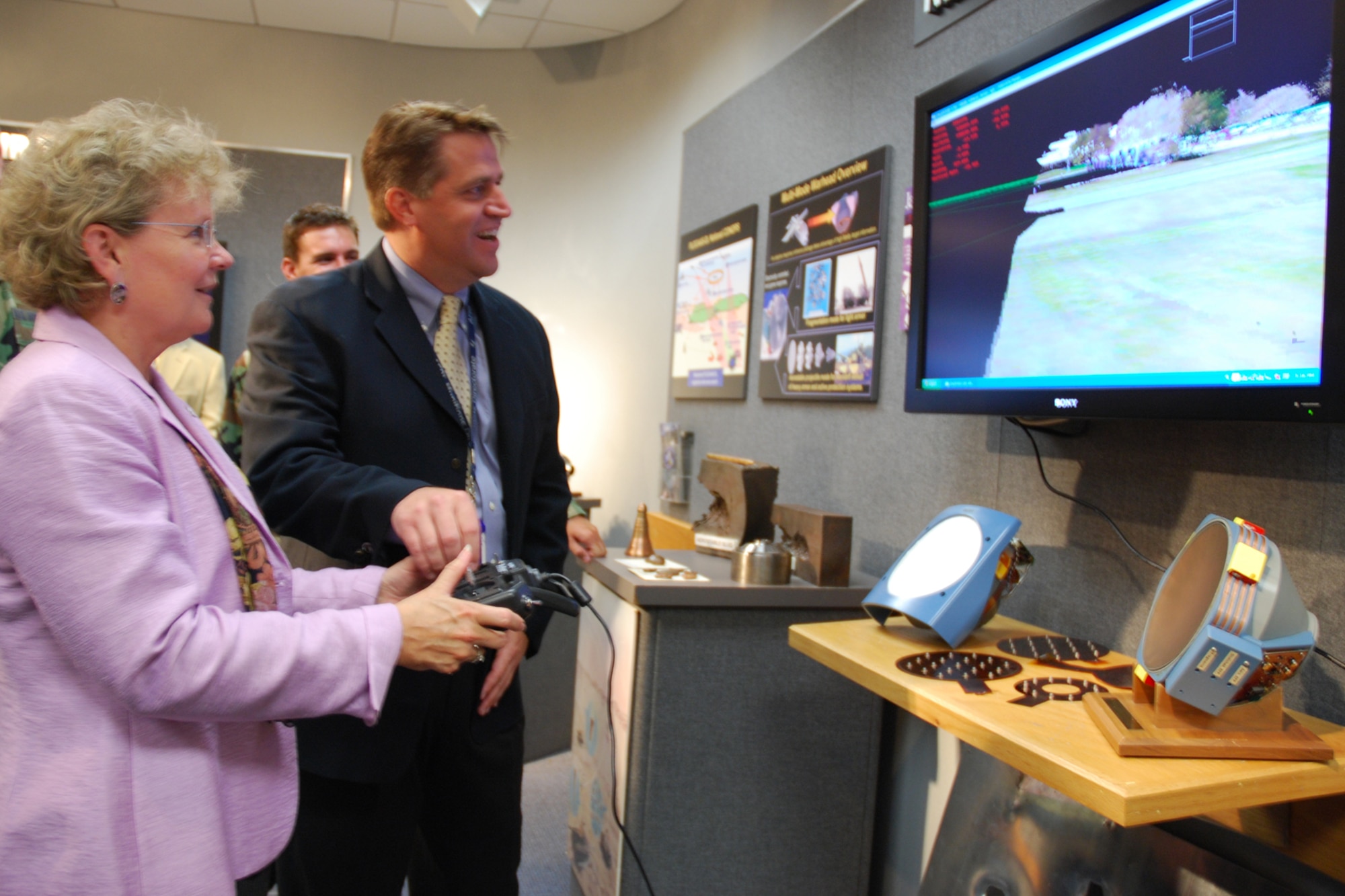 Sue Payton, Secretary of the Air Force for Acquisitions, operates a remote control at the Air Force Research Laboratory Munitions Directorate during a visit June 26, while program manager, Dr. Bill Humbert, explains the software operation. AFRL has identified Lasar Radar, or LADAR, as a sensor technology capable of providing helicopter pilots with landing zone situational awareness during brownout conditions in the desert. A brownout occurs when helicopter blades stir up sand and dust during landing, creating minimal visibility for pilot and crew. (U.S. Air Force photo by Mike Wallace)