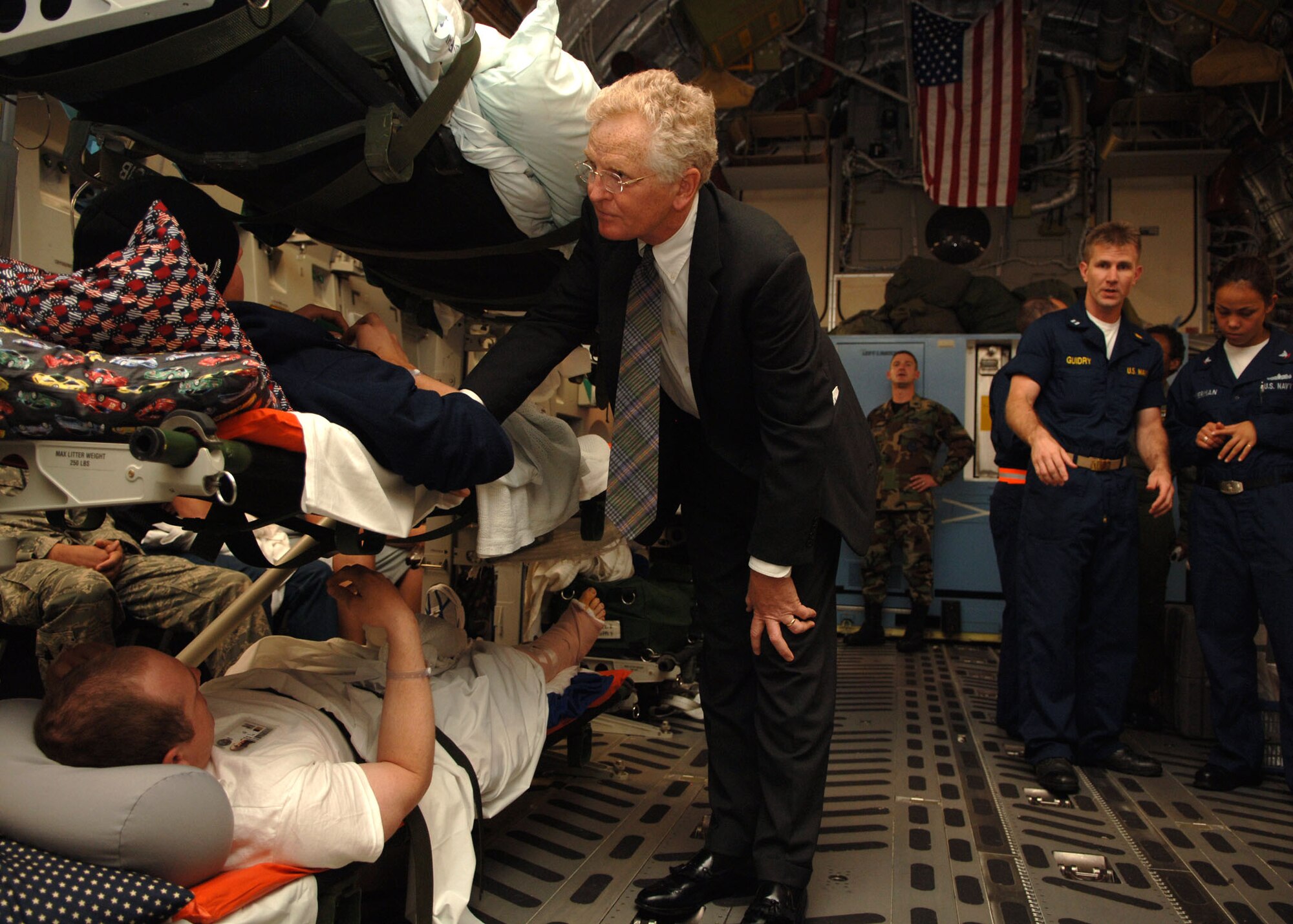 Dr. Samuel W. Casscells, Assistant Secretary for Health Affairs, talks to wounded soldiers returning from overseas as they remain strapped down on litters to prevent any further injuries during transport.