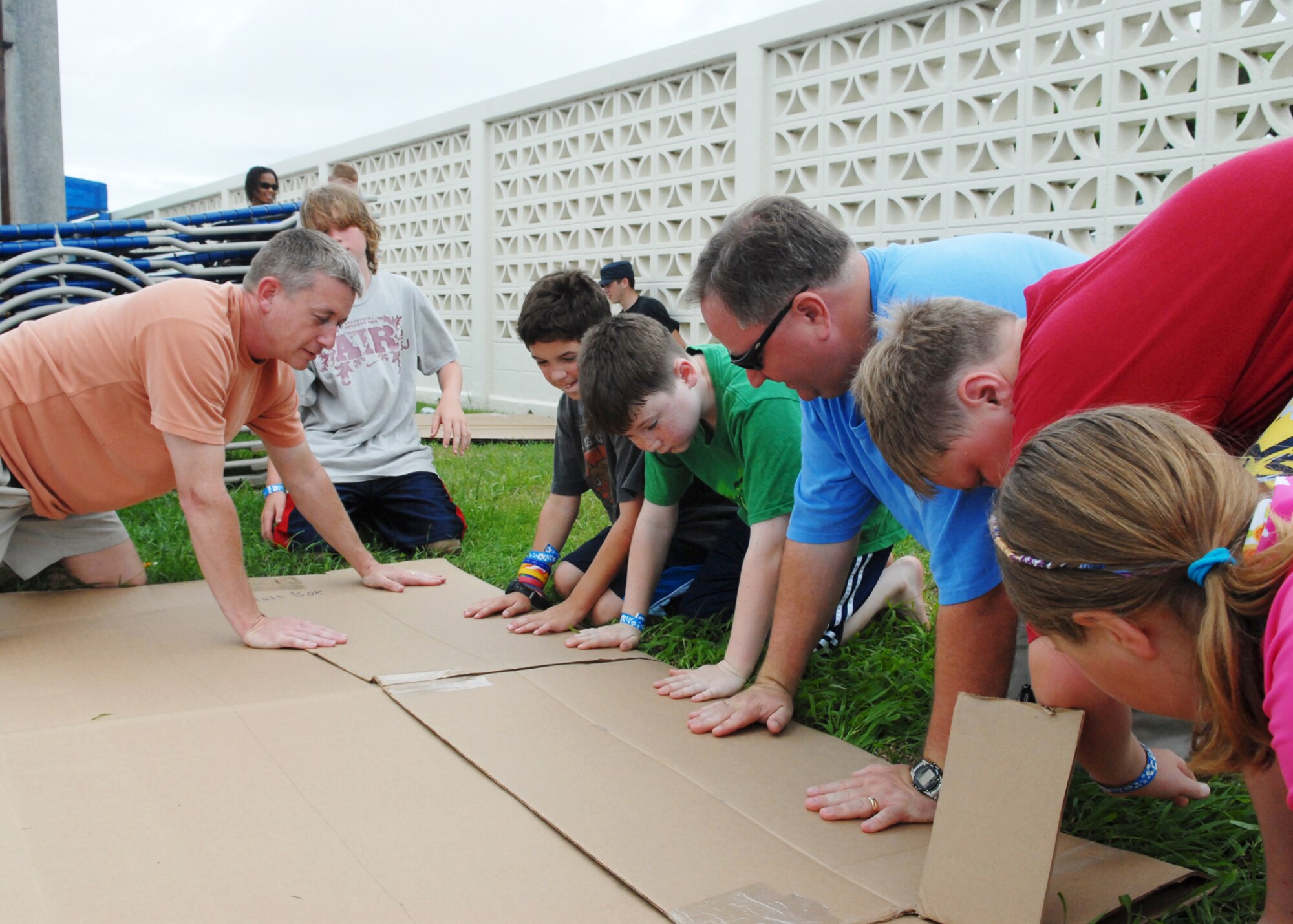 Maj. Rick Jones, 18th LRS, left, and Maj. Dave Alexander, 961st Airborne Air Control Squadron, guide their kids through the building process of their boat, the “Hammerhead,” at the cardboard boat race on Kadena Air Base, Japan, June 16. More than 50 people divided among seven teams competed. Competitors were only supplied with a roll of duct tape, three large pieces of cardboard and a cutting knife. 
U.S. Air Force photo/Senior Airman Jeremy McGuffin