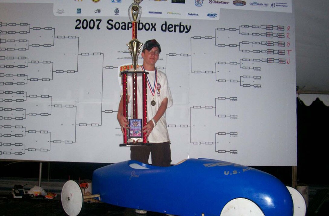 Jared Cornell standing with his hard earned trophy and his soap box car which he drove, representing the Airmen of Andersen Air Force Base. 